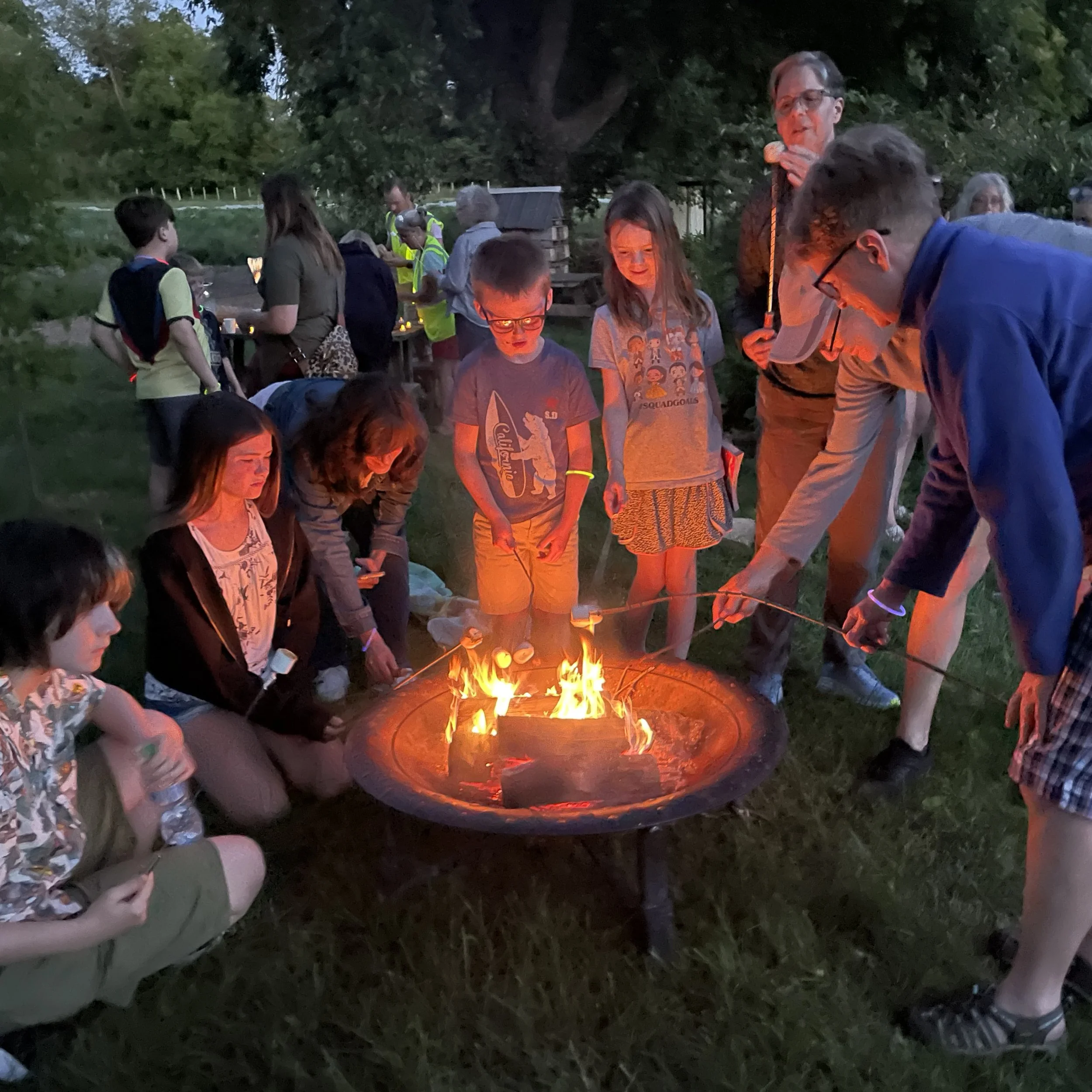 A group of children and adults roast marshmallows over a fire pit