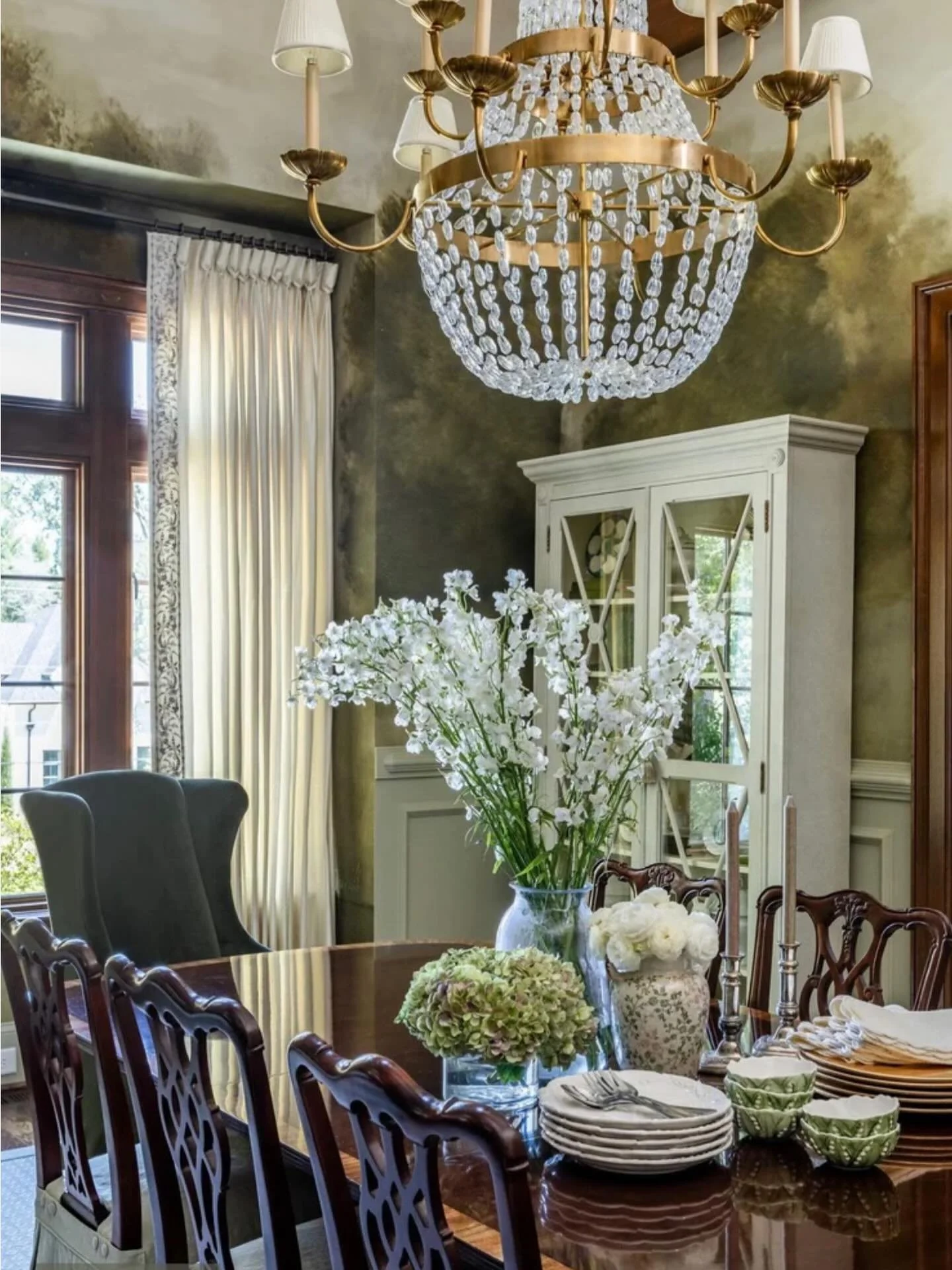 This dining room comes to life with @charlotteterrell wallpaper&mdash;moody, romantic, and perfectly balanced by warm wood tones, antique accents, and a statement chandelier by @visualcomfort . A space designed for lingering dinners and beautiful con