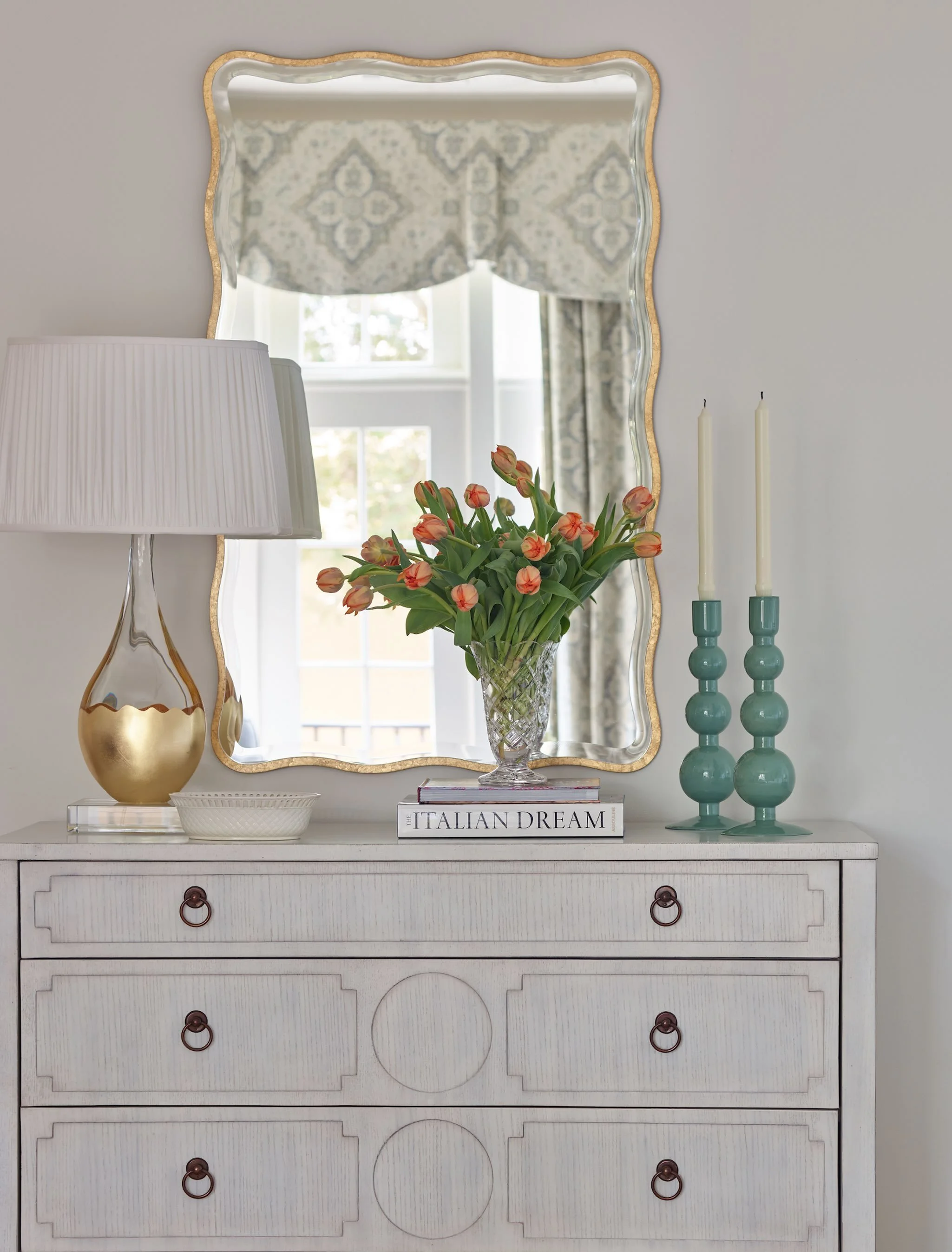 A few thoughtfully layered details can completely transform a bedroom moment.
From the sculptural mirror and soft pattern play to the fresh tulips and warm metallic accents, this vignette was designed to feel collected, calming, and quietly elegant
&