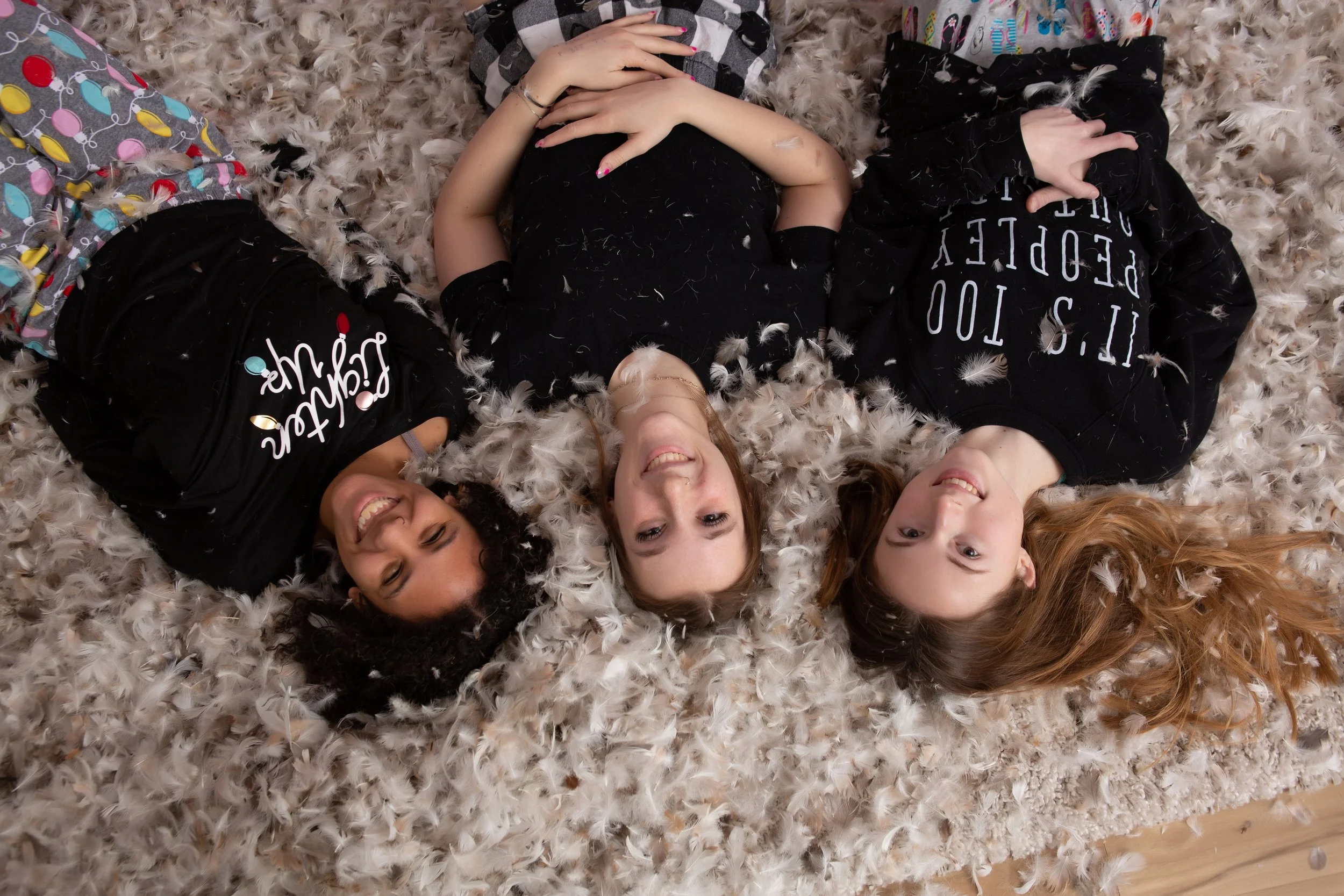 Three teenage girls laying in a pile of feathers during a Pillow Fight mini session at Adalily Photography