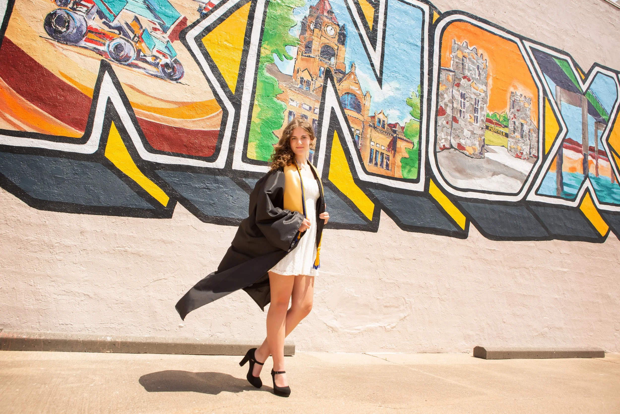 Senior Girl in her Graduation robes outside in front of the Knoxville mural