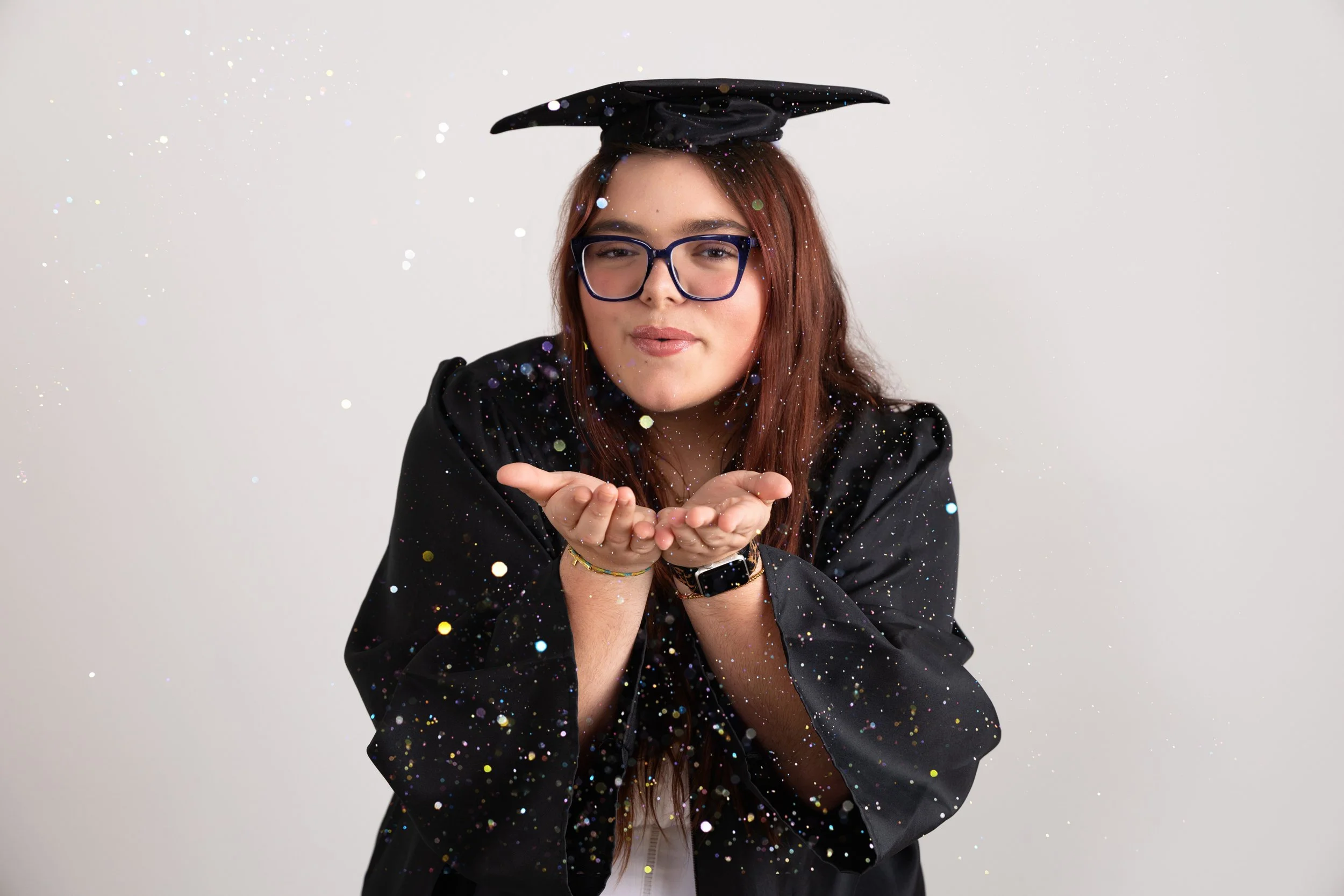 Senior Girl in her Graduation robes blowing glitter at the camera
