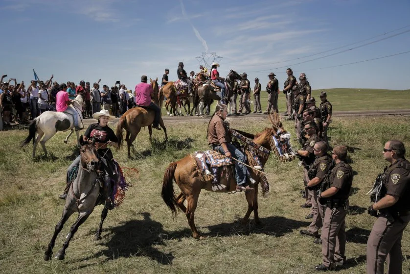 Lakota riders Alex Romero-Frederick (left) and Greg Grey Cloud (right) confront a line of North Dakota State Police the day that construction crews began work on the Dakota Access Pipeline just outside the Standing Rock Reservation, on August 15, 2016. The display was part of a ceremonial horse introduction meant to be peaceful. photo: Daniella Zalcman