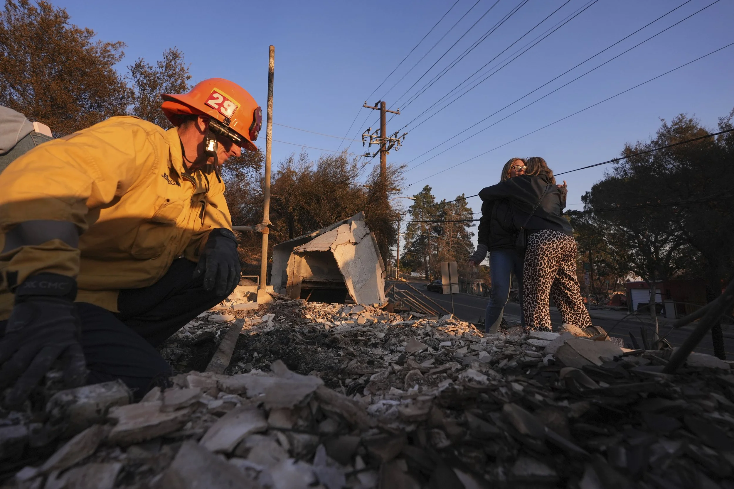  Glendale Fire Department captain Chris Jernegan, left, searches through debris as his wife Alison, center, hugs Brynna Venne after Brynna's home was destroyed by the Eaton Fire in Altadena, Calif., Saturday, Jan. 11, 2025. (AP Photo/Mark J. Terrill)