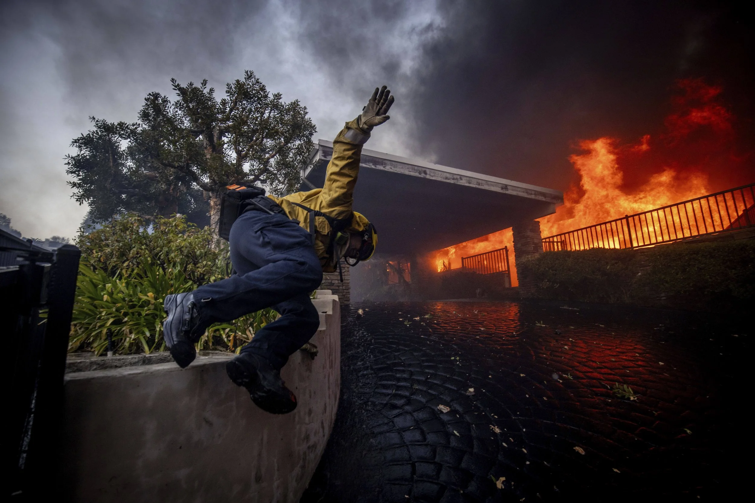  A firefighter jumps over a fence while fighting the Palisades Fire in the Pacific Palisades neighborhood of Los Angeles, Tuesday, Jan. 7, 2025. (AP Photo/Ethan Swope) 