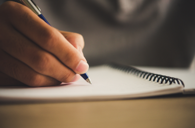 A person writing with a pen in a spiral notebook