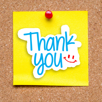 Thank you written on a yellow Post-It Note, pinned to a cork board, with a red smiley face