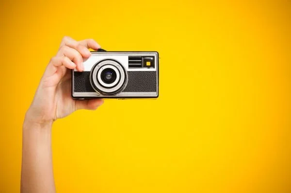 A person holding a vintage camera with a bring yellow background