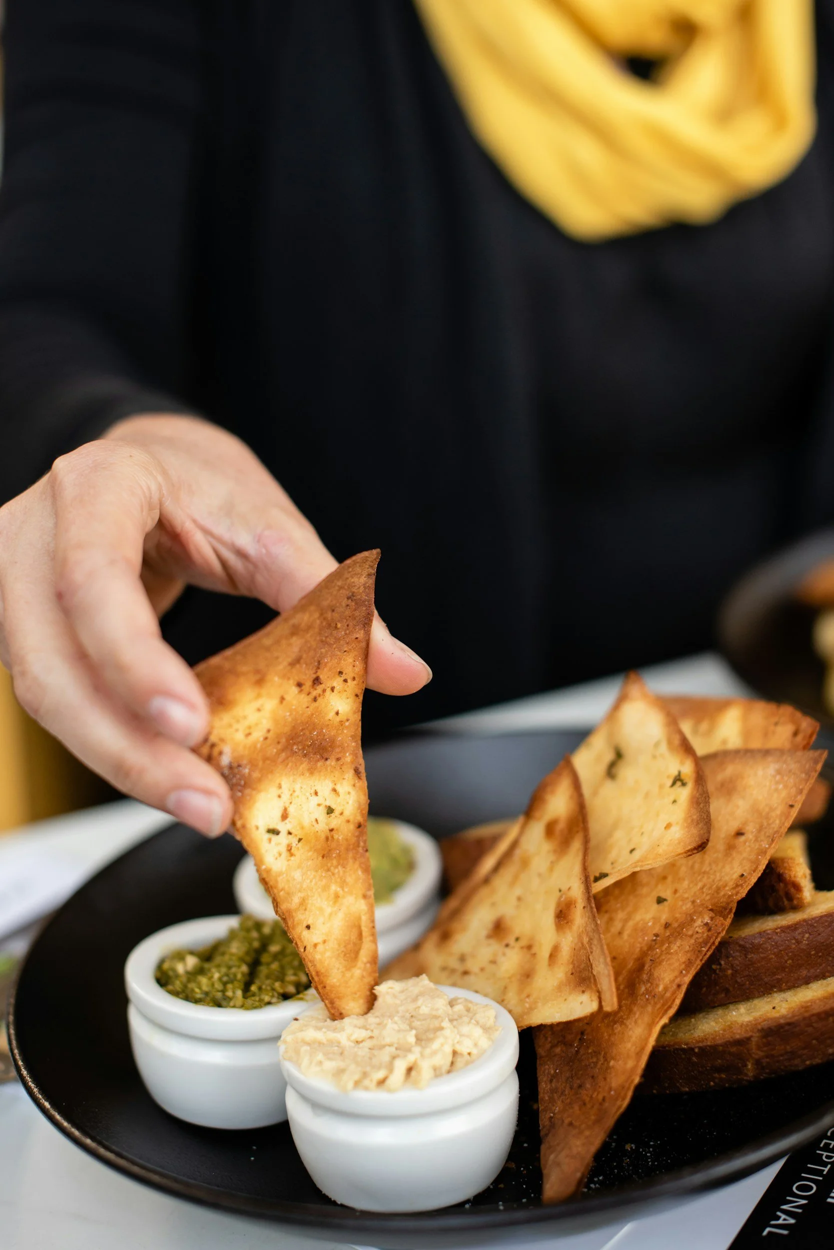 Hand holding a piece of bread beside a bowl of dip.