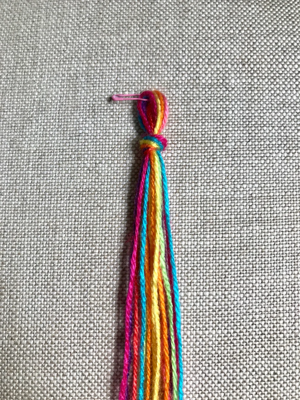 1. Cut a 72”/183cm length of each color. Fold all strands in half and tie a knot near the top, leaving a loop for the closure. Secure to a table with tape, or to the fabric of a pillow or your jeans with a safety pin.