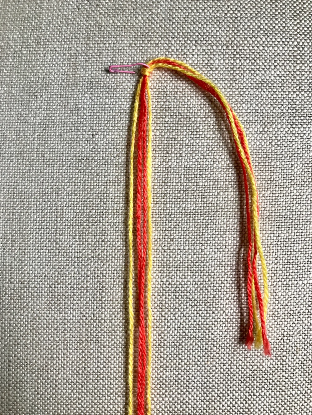 1. Cut two strands each of two colors, 36”/91cm long. Tie a knot, leaving 6”/15cm long tail ends. Secure to a table with tape, or to the fabric of a pillow or your jeans with a safety pin.