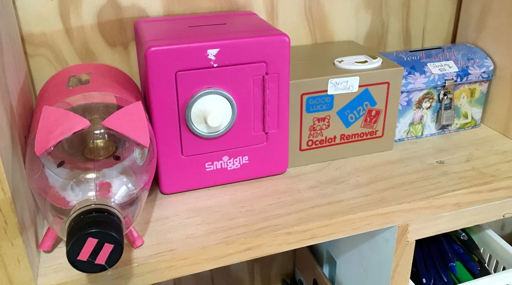 Her piggy bank and money boxes sitting on the shelf.