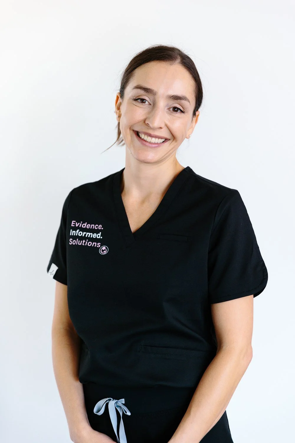Jamie Mueller smiling in black scrubs against a pale background.
