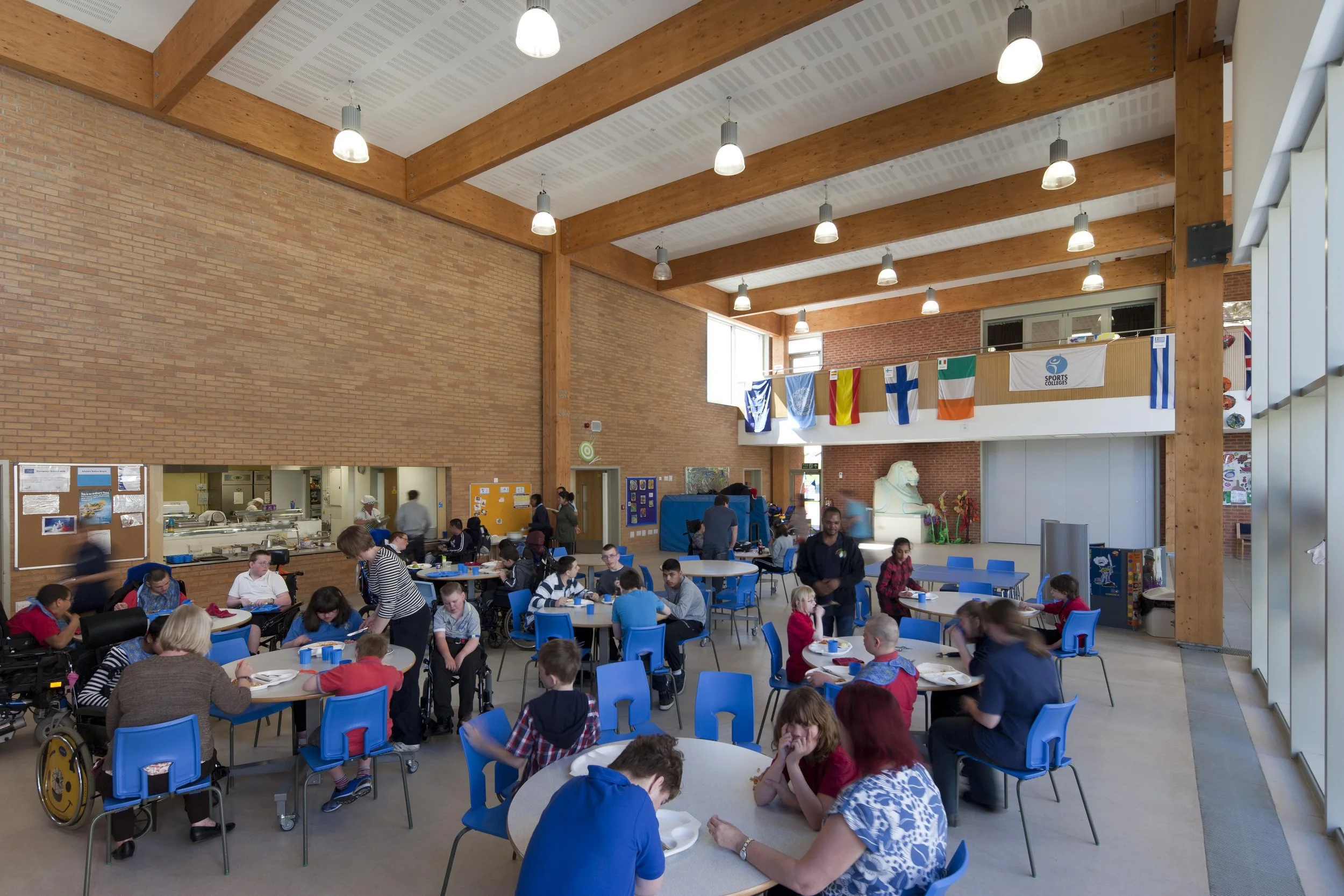 Light-filled central atrium heart space at Oak Field School featuring exposed structural timber framing and views of the sensory courtyard.