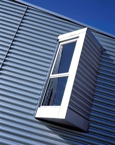 Close-up of a modern building's aluminum siding with a protruding rectangular window set at an angle, against a clear blue sky.