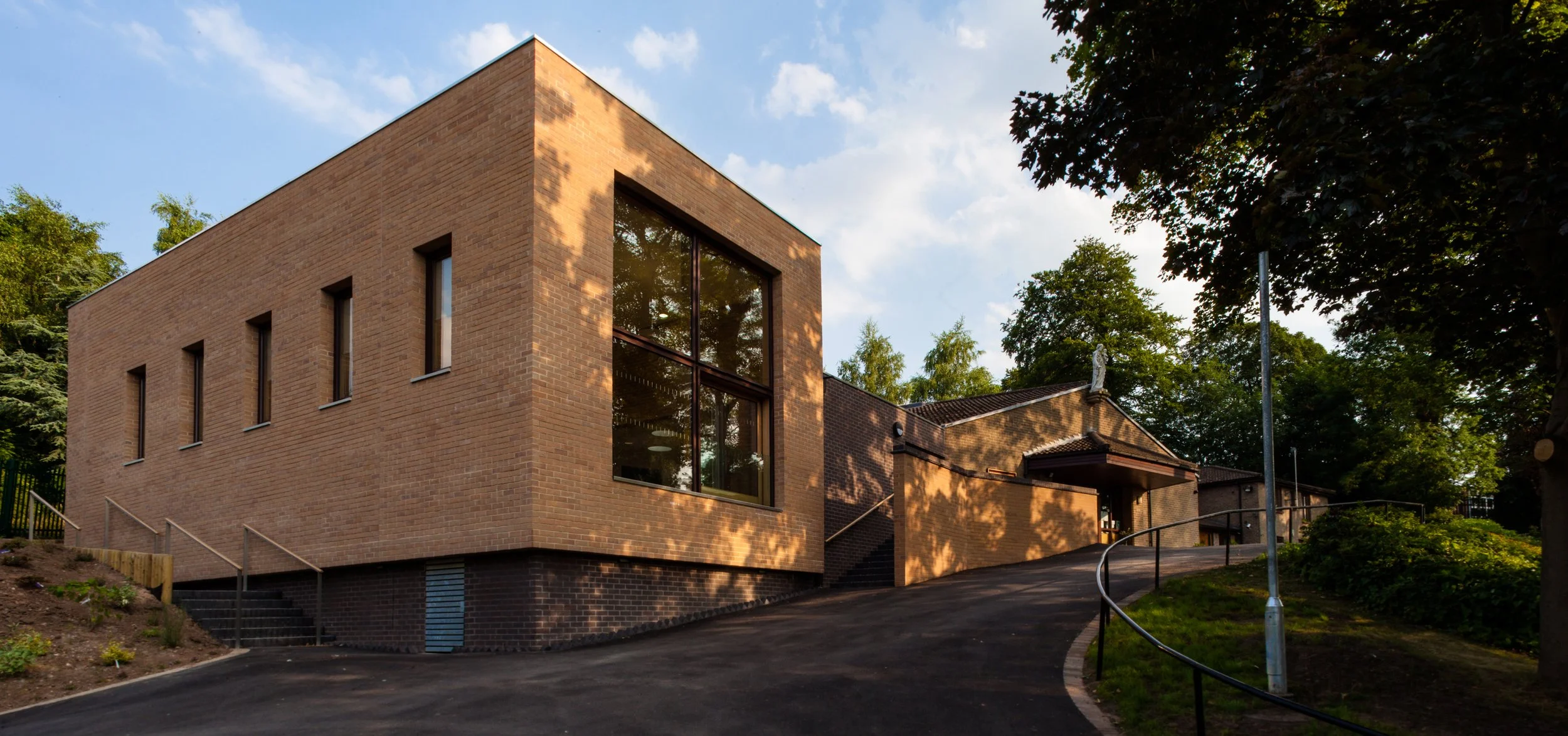 Exterior view of St Josephs Church Hall Derby showing large picture window and warm brick facade on a sloping site.