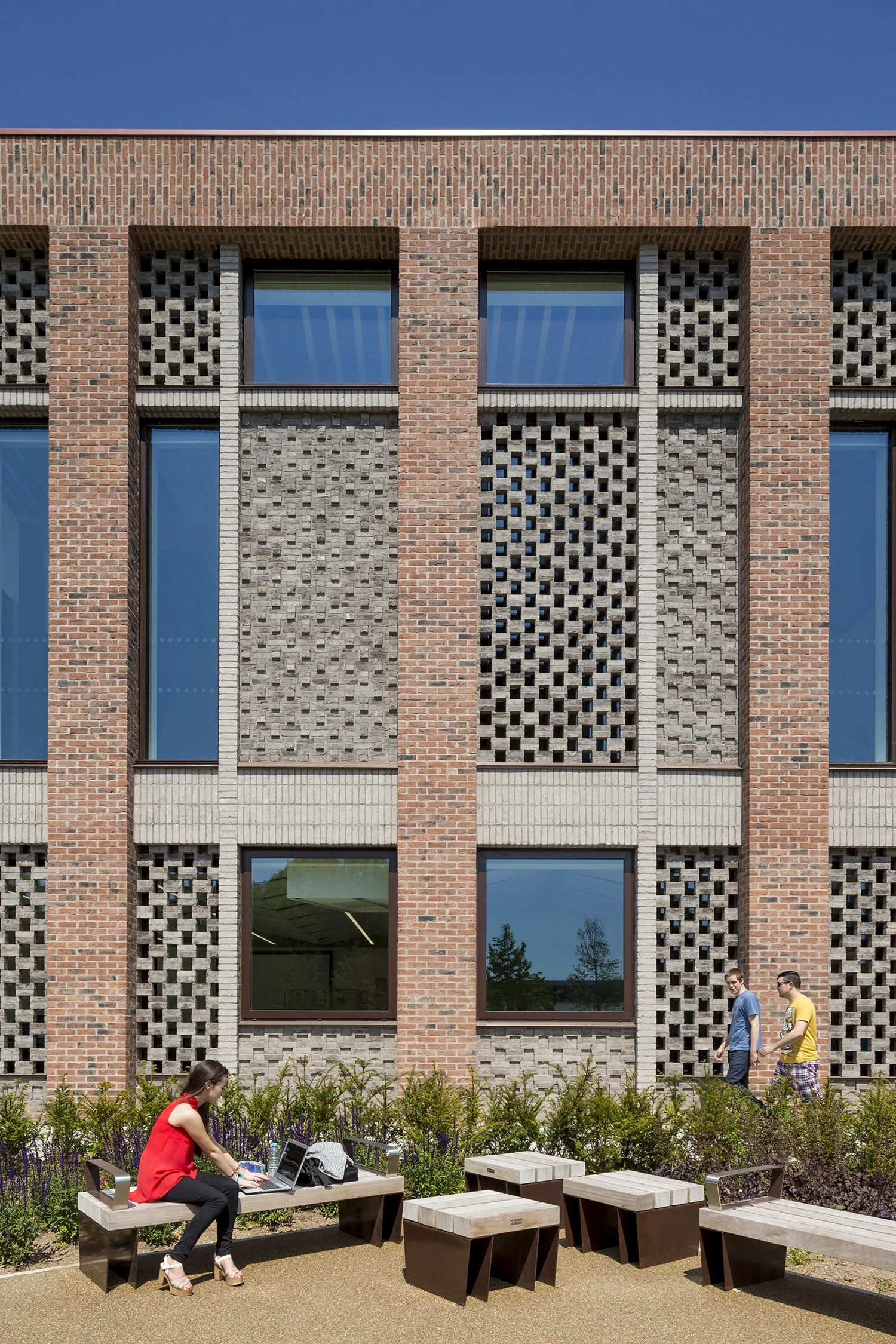Women working on laptops at outdoor benches with a modern brick building in the background.