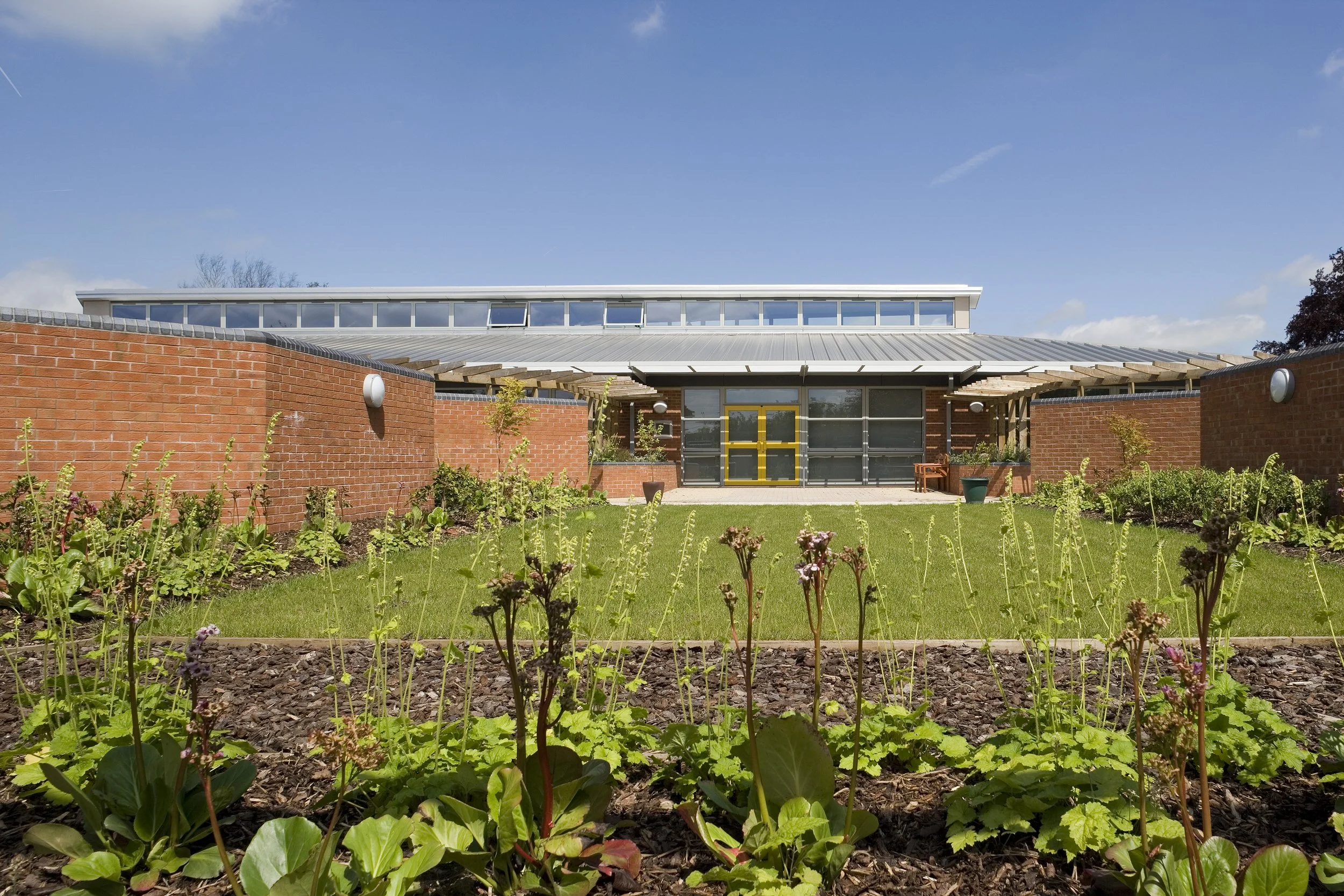 Walled Moorish-inspired sensory garden featuring wide resin-bound gravel footpaths, timber pergolas, and raised planting beds.