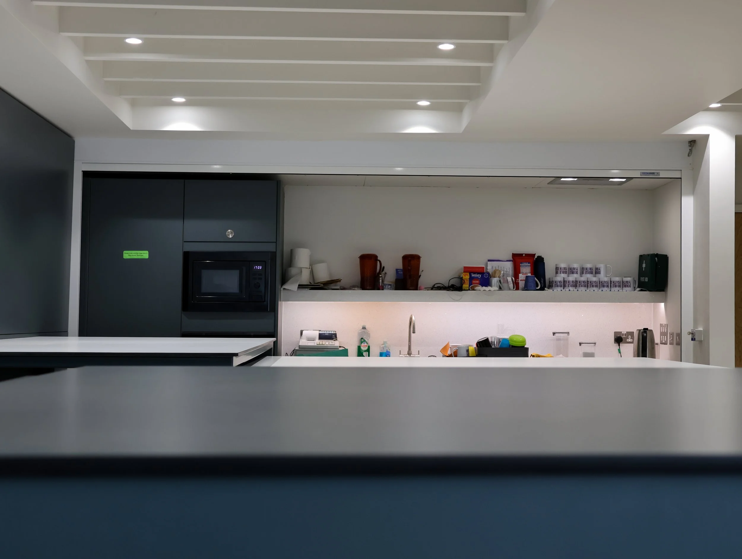 Interior view of the kitchen and bar space at Double Six Youth Club, featuring integrated equipment and storage space, with comfortable energy efficient lighting.