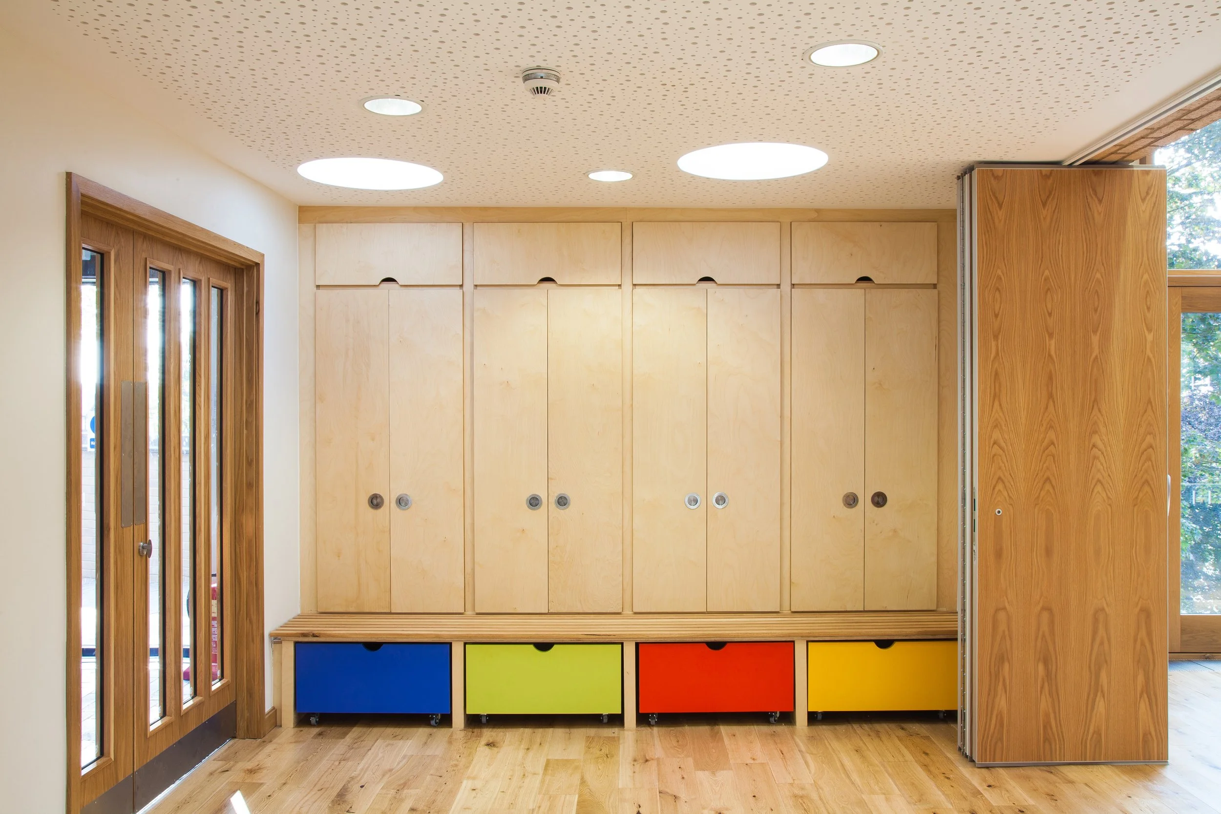 Interior view of a room with wooden cabinets and colorful storage drawers, a wooden door with glass panels, and a window letting in natural light.