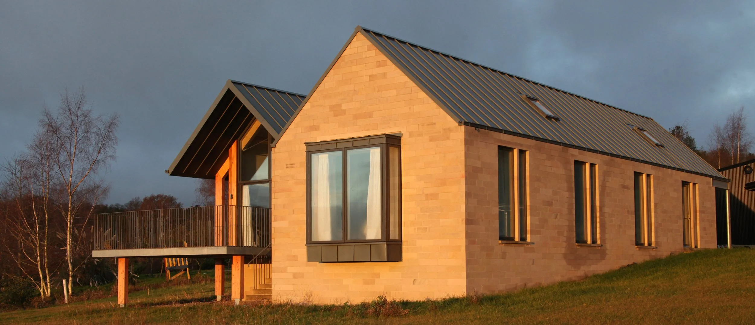 Exterior view of local coursed Derbyshire gritstone walling paired with dark grey metal window frames.