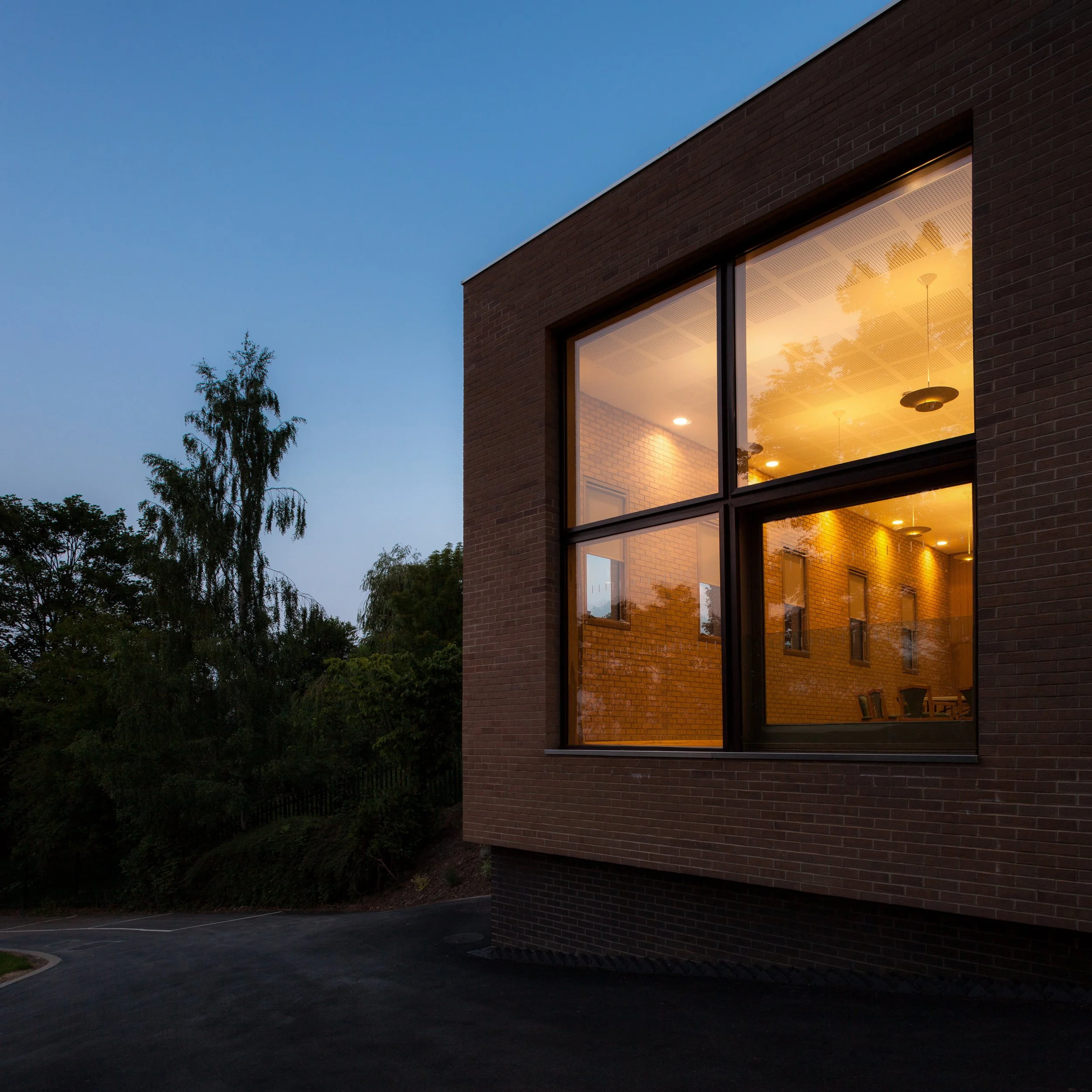 Evening shot of St Josephs Church Hall in Derby illuminated from within against mature surrounding trees.