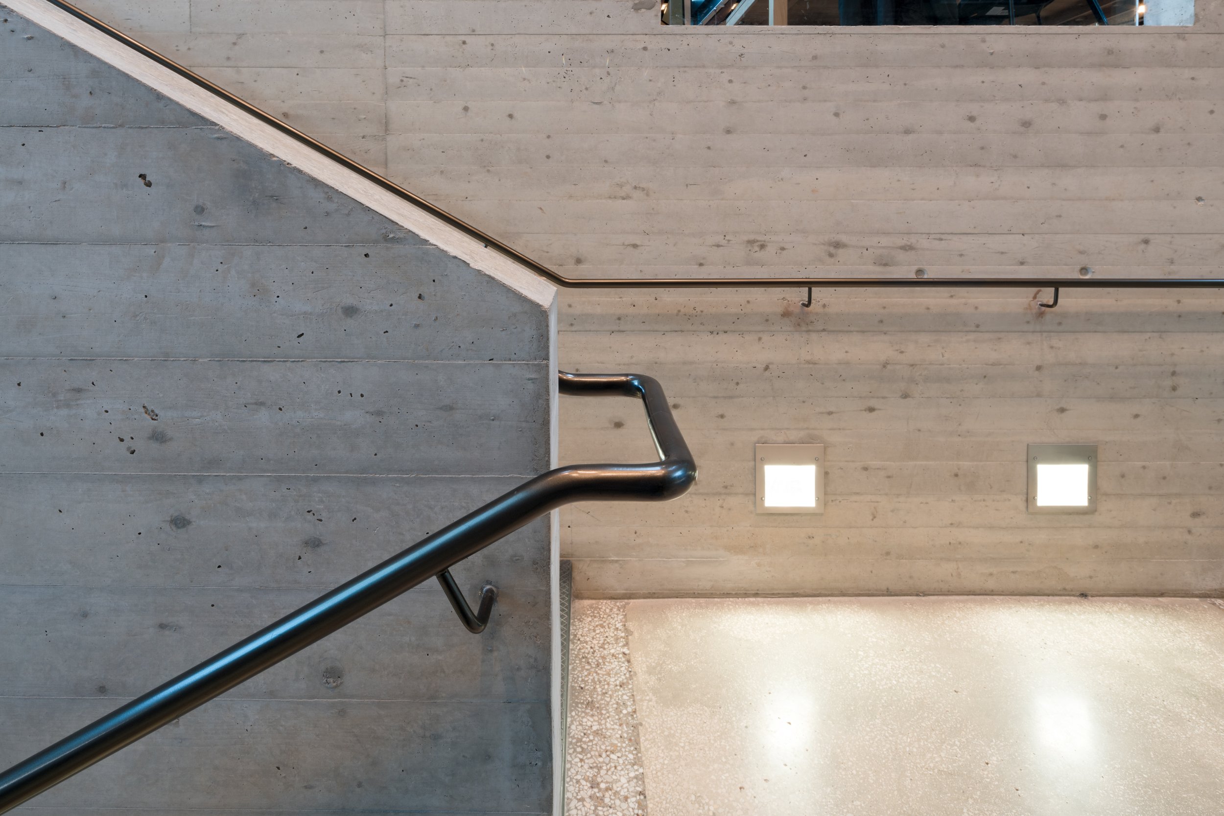 The image shows concrete stairs with a metal handrail against a wall with two square lights.