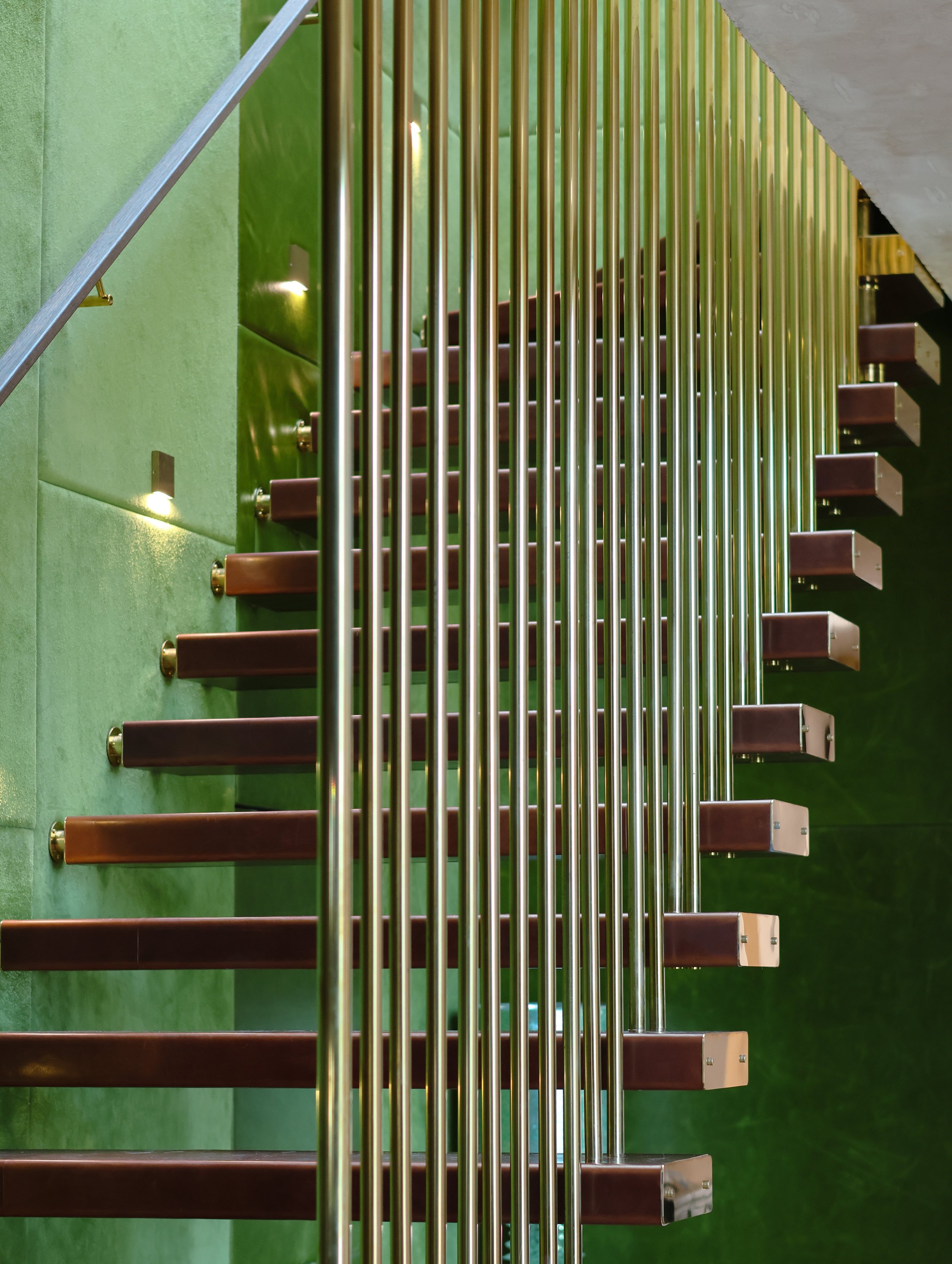 Staircase with brown steps, green wall, and metallic handrails inside building.