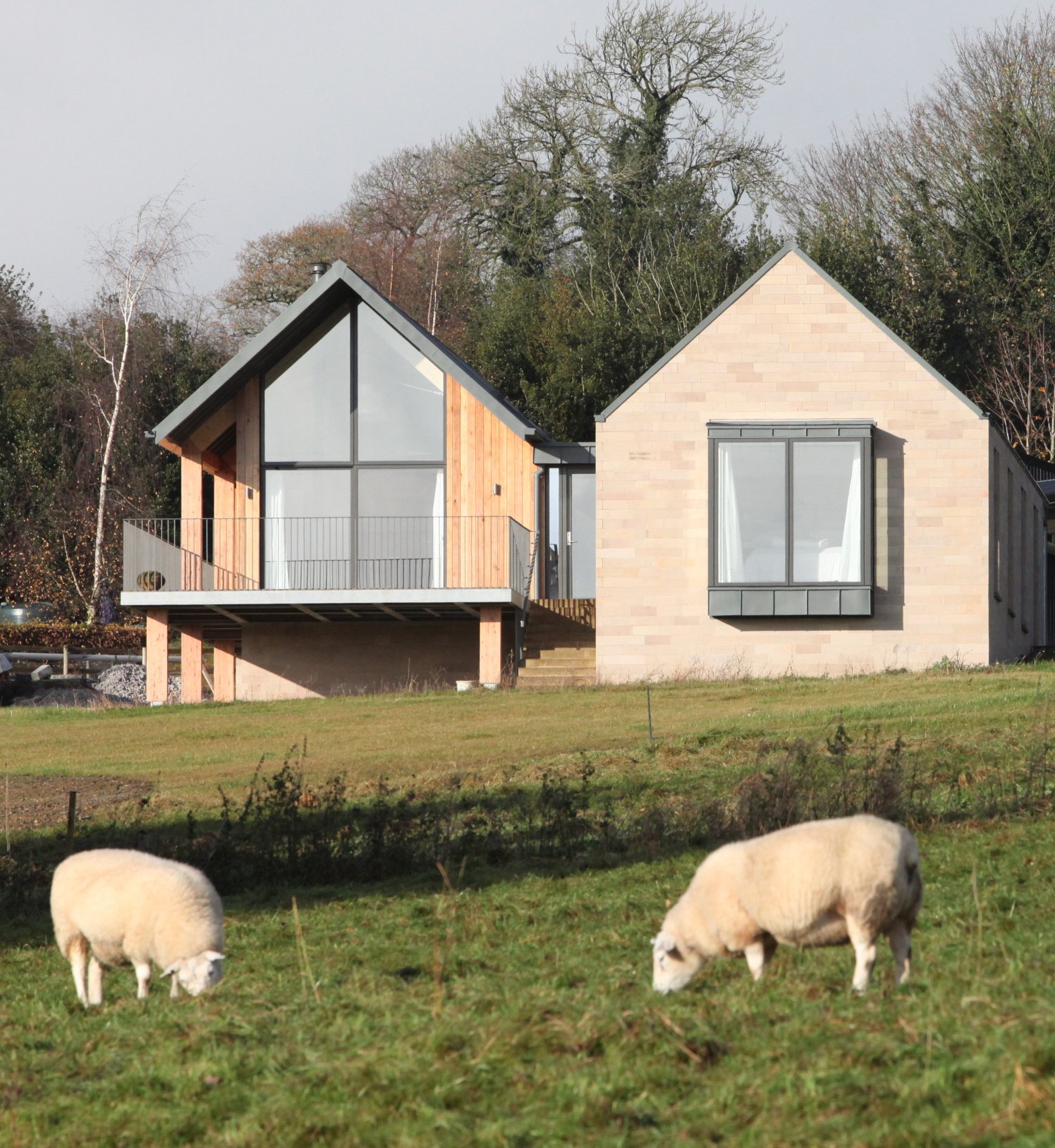 Modern barn-style home showing parallel stone and timber gabled wings connected by a flat-roofed central spine.