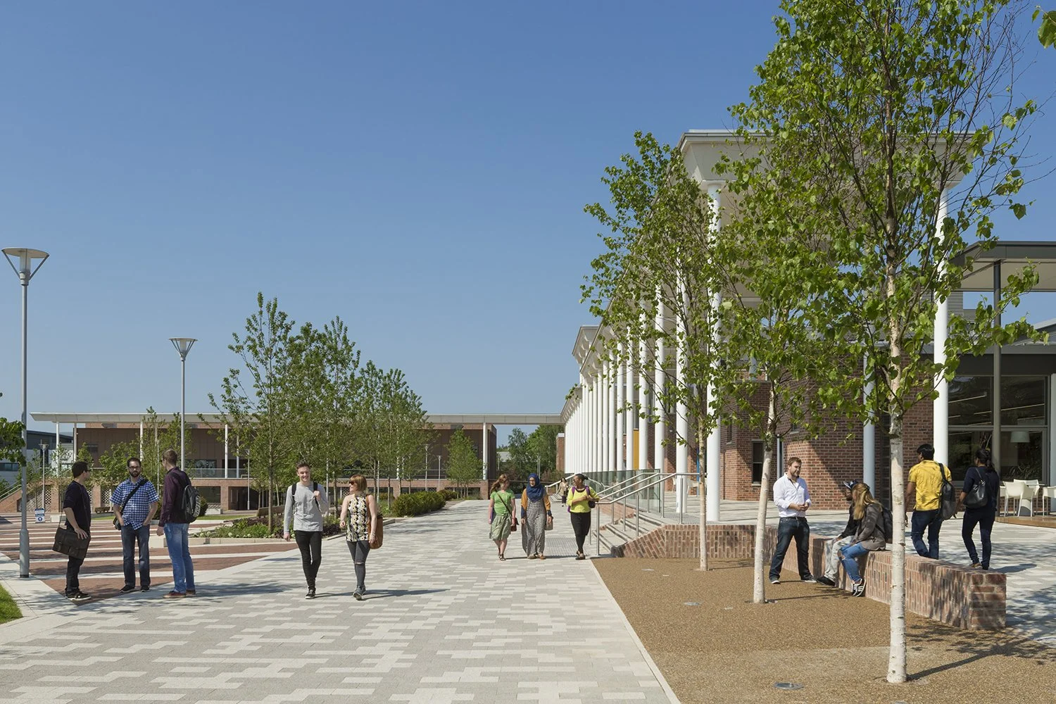 Landscaped campus plaza framing the glazed entrance of the Heart of Campus mixed-use educational building