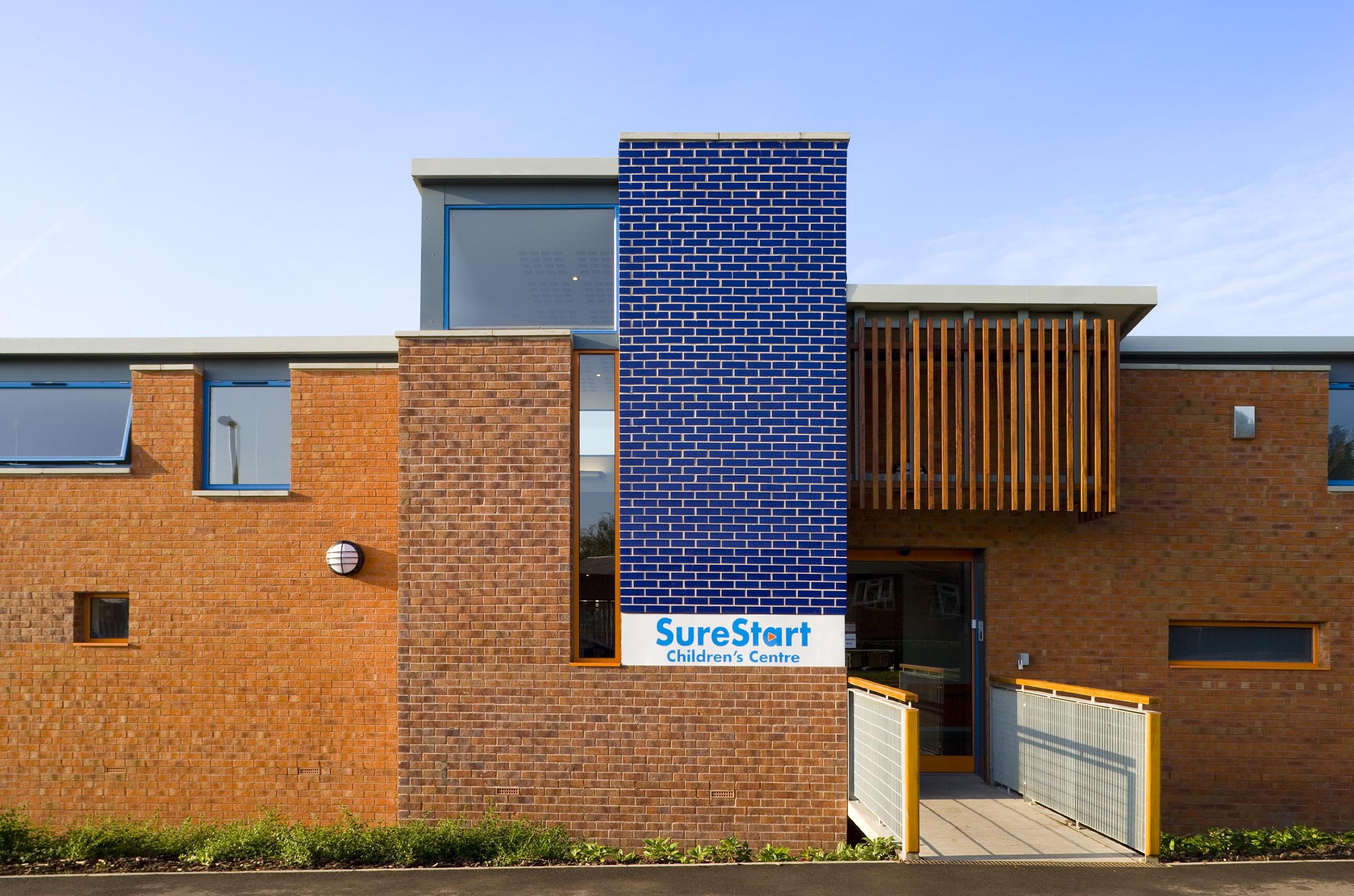 Modern brick and blue panel children's centre building with a sign that reads 'SureStart Children's Centre'