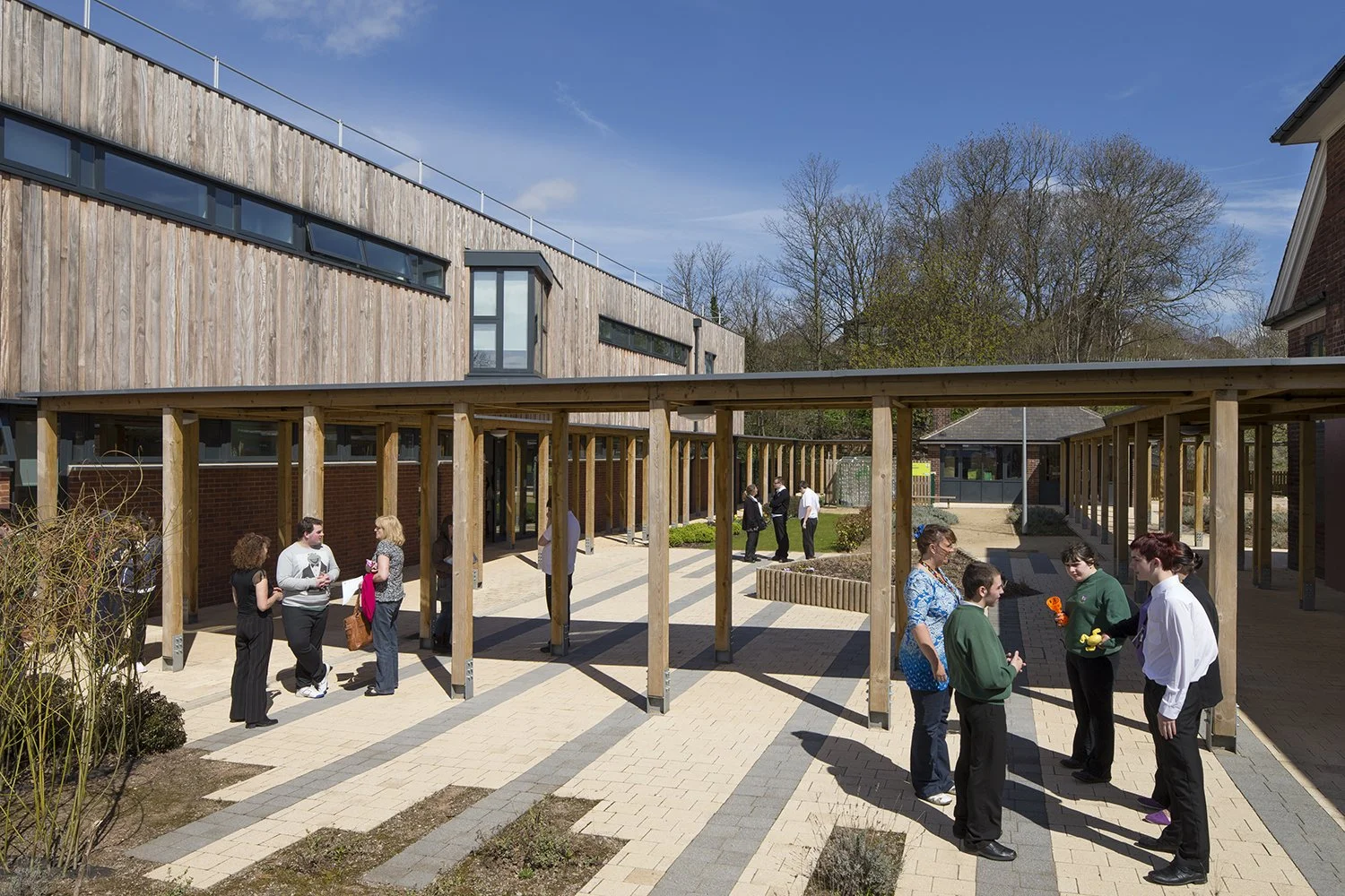 Exterior facade of Rosehill School in Nottingham showcasing red brick retaining walls, vertical timber cladding, and green roofs.