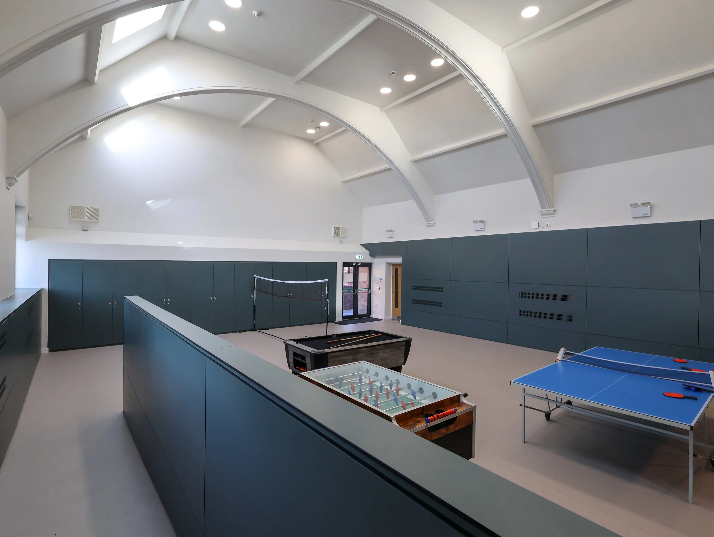 Interior view of the double-height main hall at Double Six Youth Club, featuring exposed timber arch trusses and high-level natural lighting.