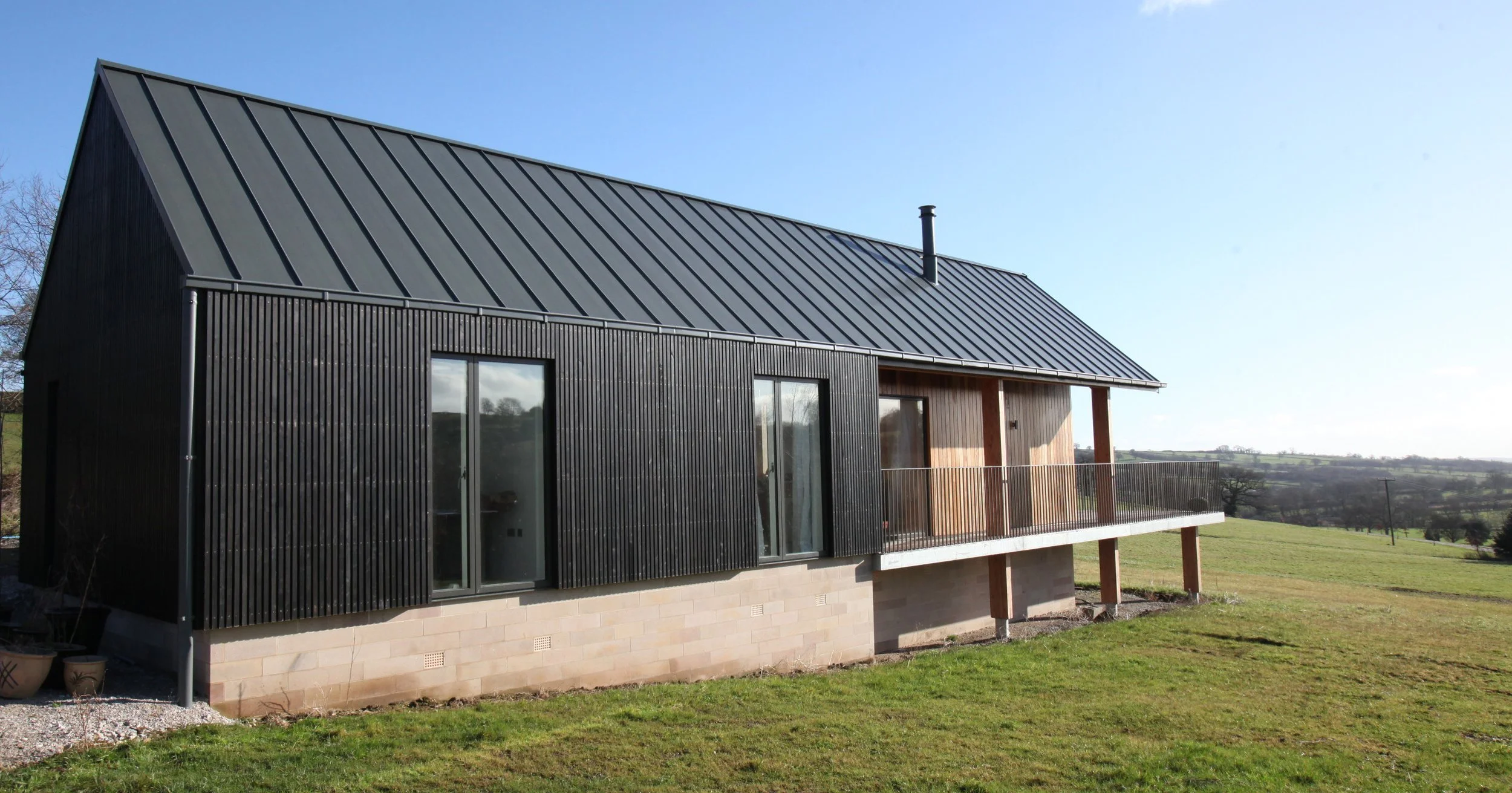 Contemporary timber-clad gable and stone barn volume at Alton Nether Farm in Kirk Ireton set against a sloped rural landscape.
