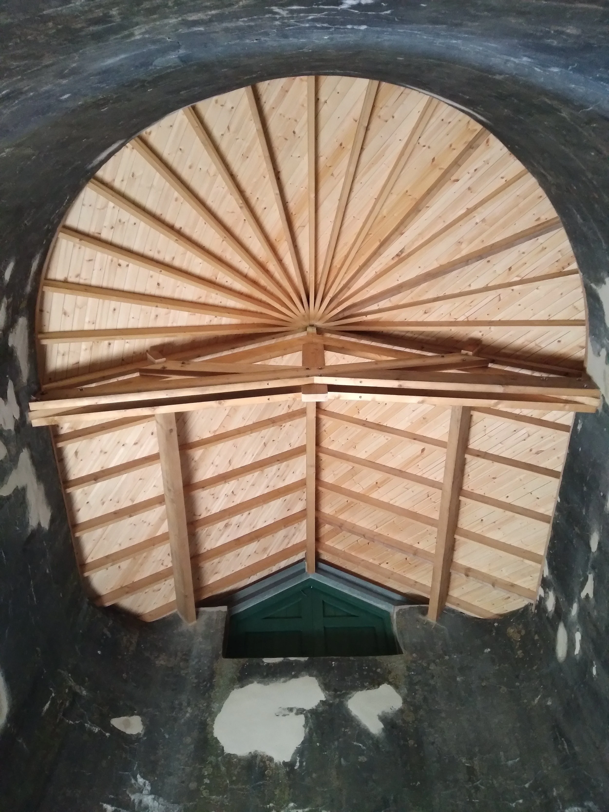 Looking through a circular opening to a vaulted wooden ceiling with wooden beams.