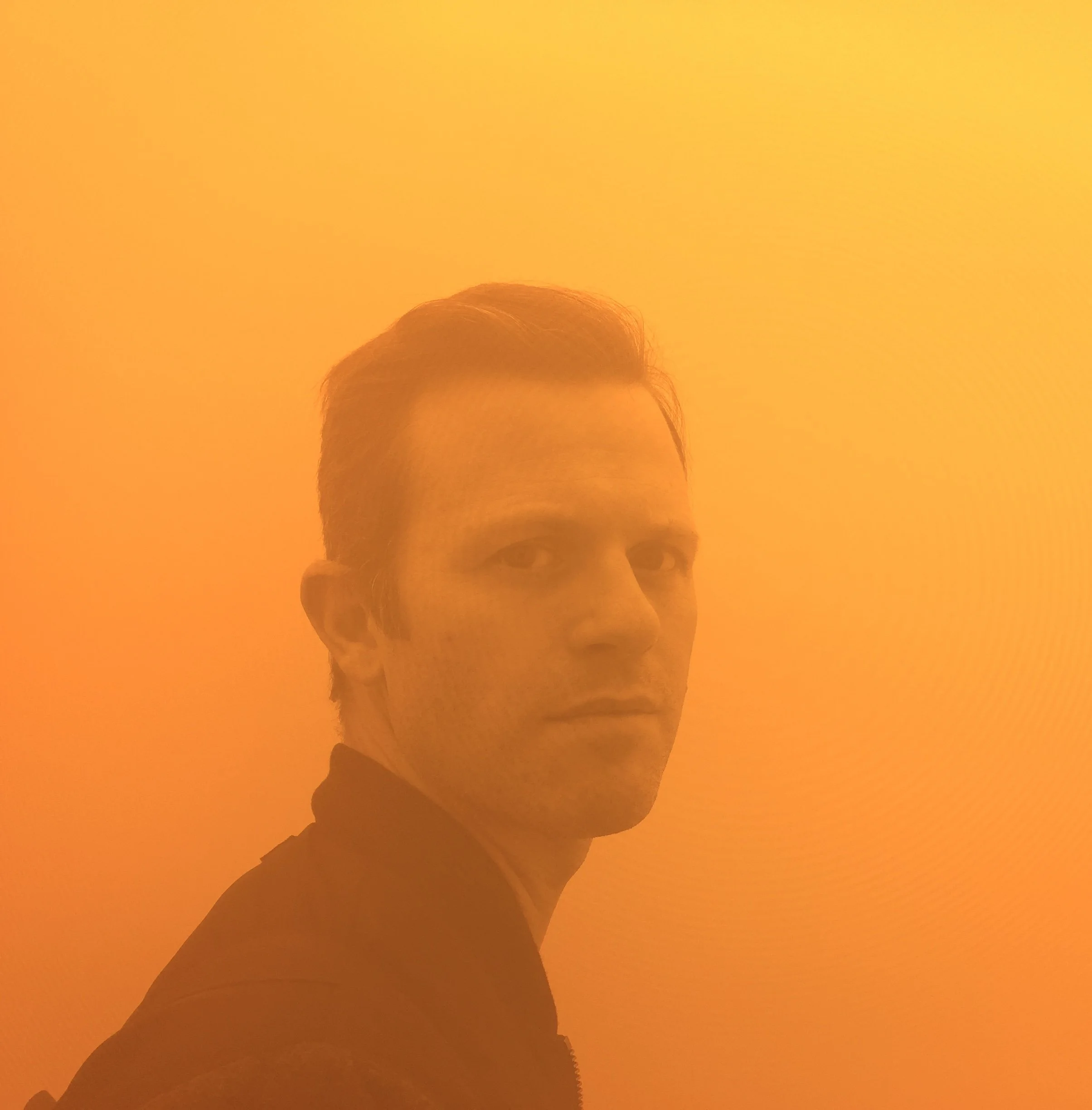 Portrait of a man with short dark hair against an orange background.