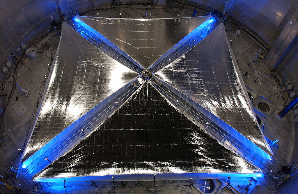 A 20-meter solar sail and boom system, developed by ATK Space Systems of Goleta, Calif., is fully deployed during testing at NASA Glenn Research Center's Plum Brook facility in Sandusky, Ohio. Blue lights positioned beneath the system help illuminate the four triangular sail quadrants as they lie outstretched in Plum Brook's Space Power Facility -- the world's largest space environment simulation chamber. The sail material is supported by a series of coilable booms, which are extended via remote control from a central stowage container about the size of a suitcase, and is made of an aluminized, plastic-membrane material called CP-1. The material is produced under license by SRS Technologies of Huntsville, Ala. The deployment, part of a series of tests in April, is a critical milestone in the development of solar sail propulsion technology that could lead to more ambitious inner Solar System robotic exploration. Image credit: NASA