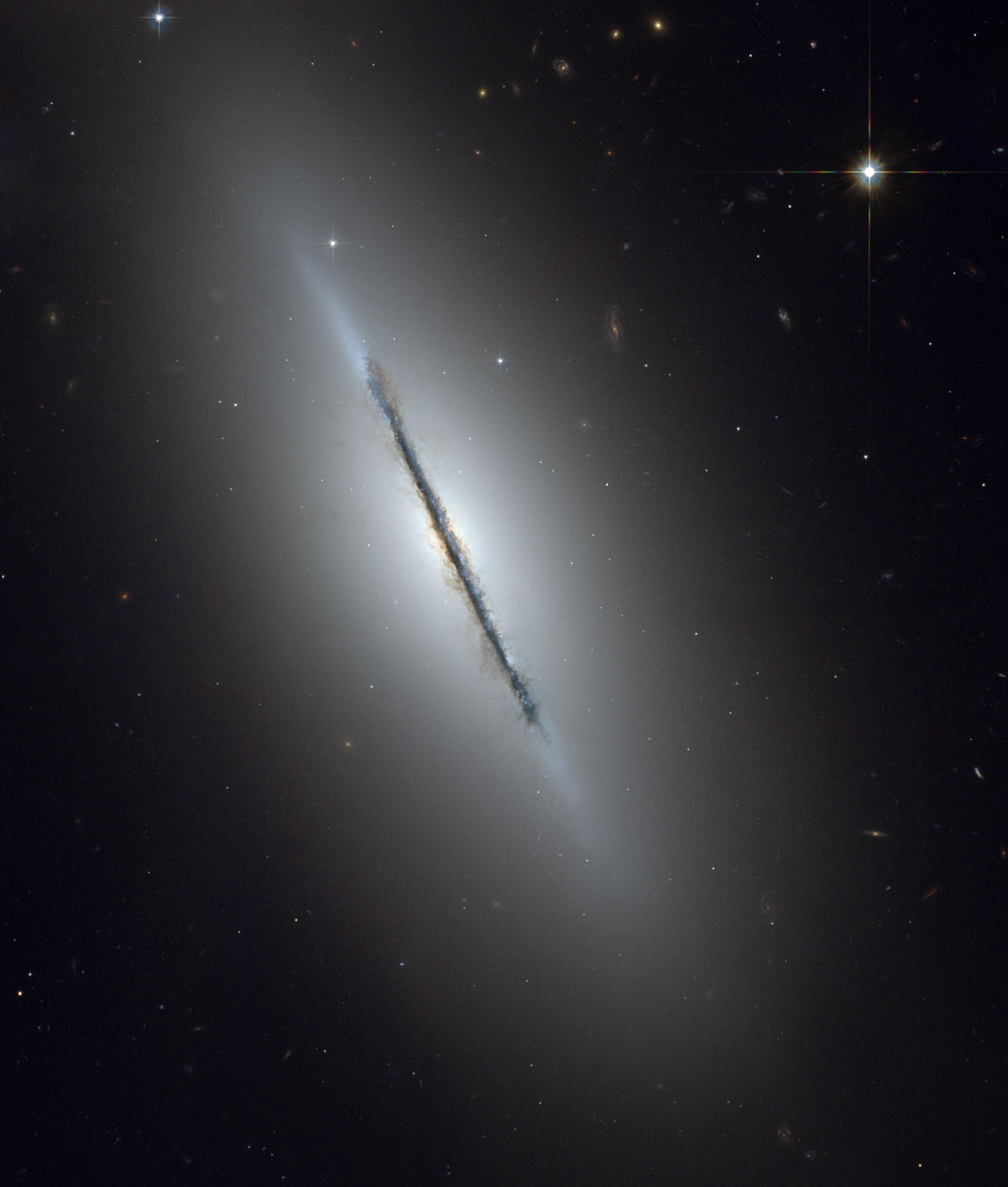 The disk galaxy NGC 5866 tilted nearly edge-on to our line-of-sight. Hubble's sharp vision reveals a crisp dust lane dividing the galaxy into two halves. The image highlights the galaxy's structure: a subtle, reddish bulge surrounding a bright nucleus, a blue disk of stars running parallel to the dust lane, and a transparent outer halo. Image credit: NASA, ESA, and The Hubble Heritage Team (STScI/AURA)