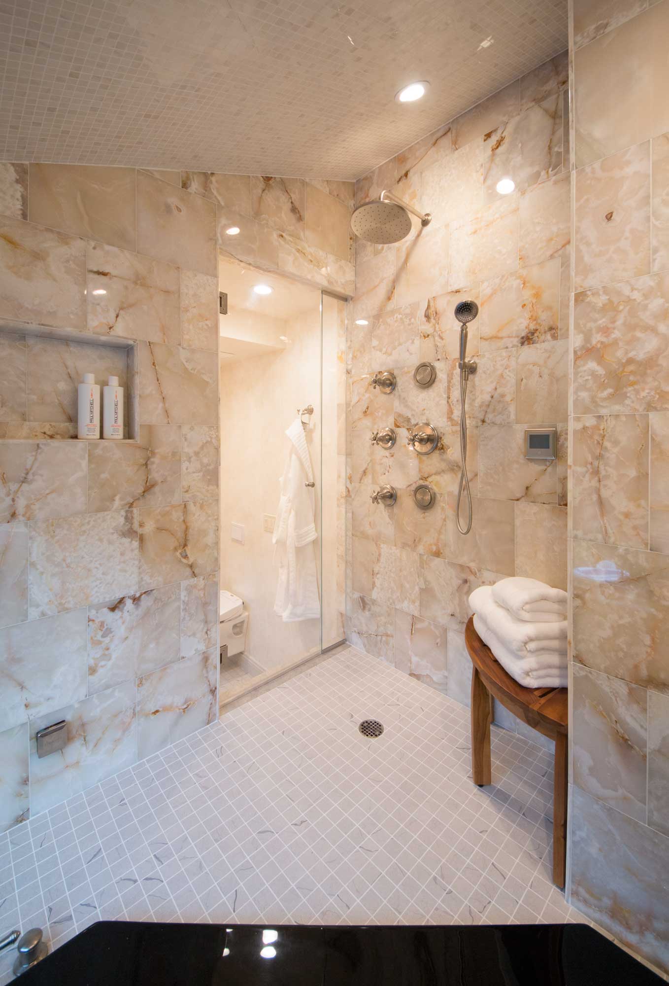 Some of the technology we incorporated into the space includes ... invisible speakers and a television that serves as a mirror when powered off; radiant heat flooring, mirror defogger, state of the art bidet seat, body sprays, two hand showers, rain shower and a Lutron home automation system that is controlled wirelessly. This master bathroom incorporates a sunken soaking tub and a steam shower spa system with aroma therapy, chroma therapy, and invisible speakers system for a total mind and body experience. 