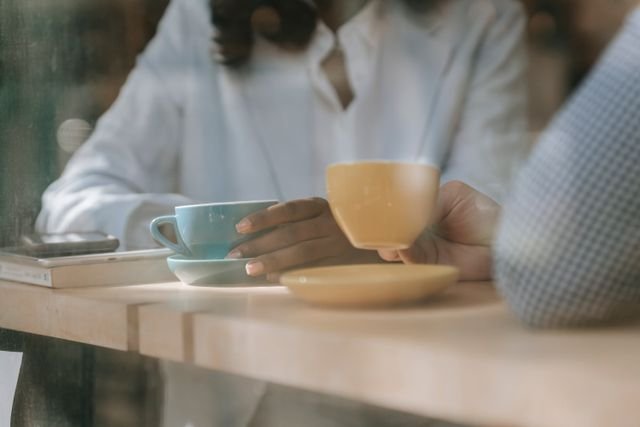Two people sitting at a counter drinking coffee, just the mid section of their body and their coffee cups are showing