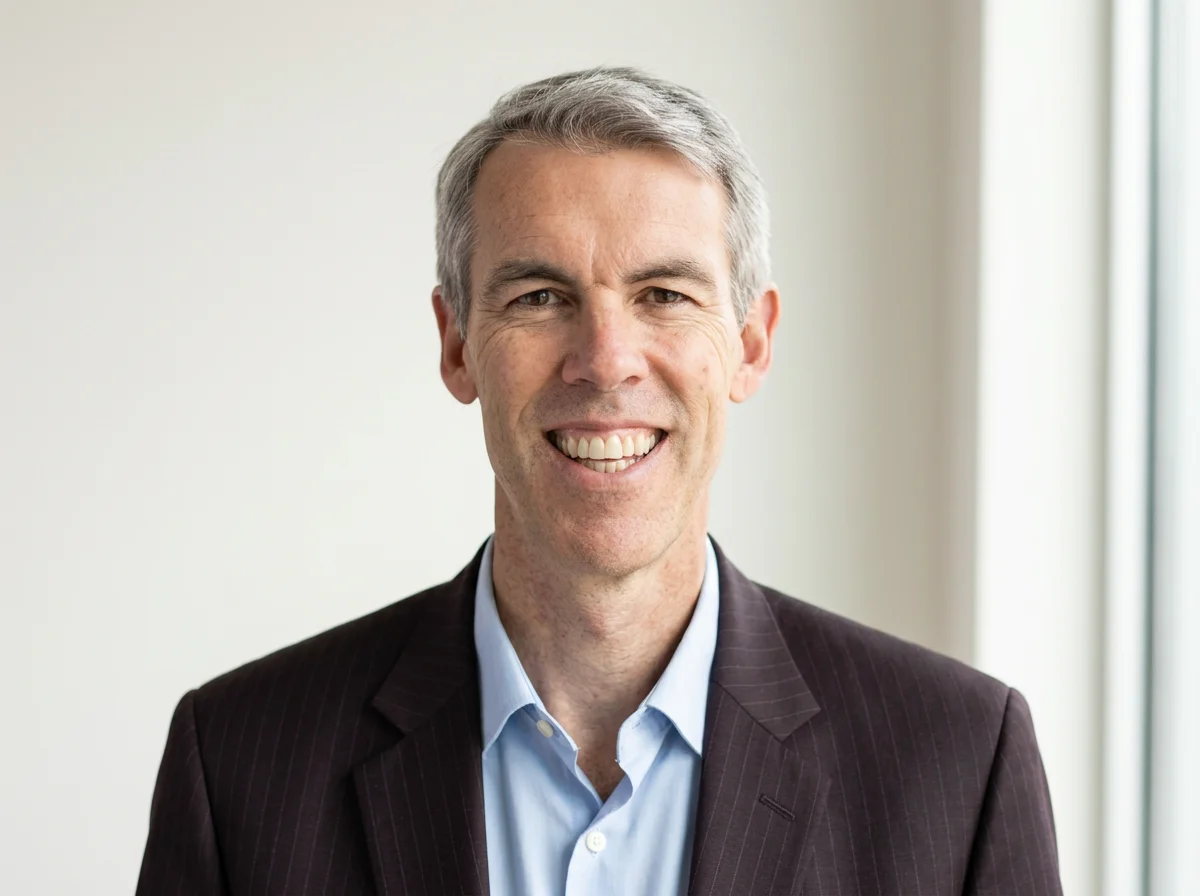 Portrait of Nick Petrie smiling, dressed in a dark pinstripe suit and light blue shirt.