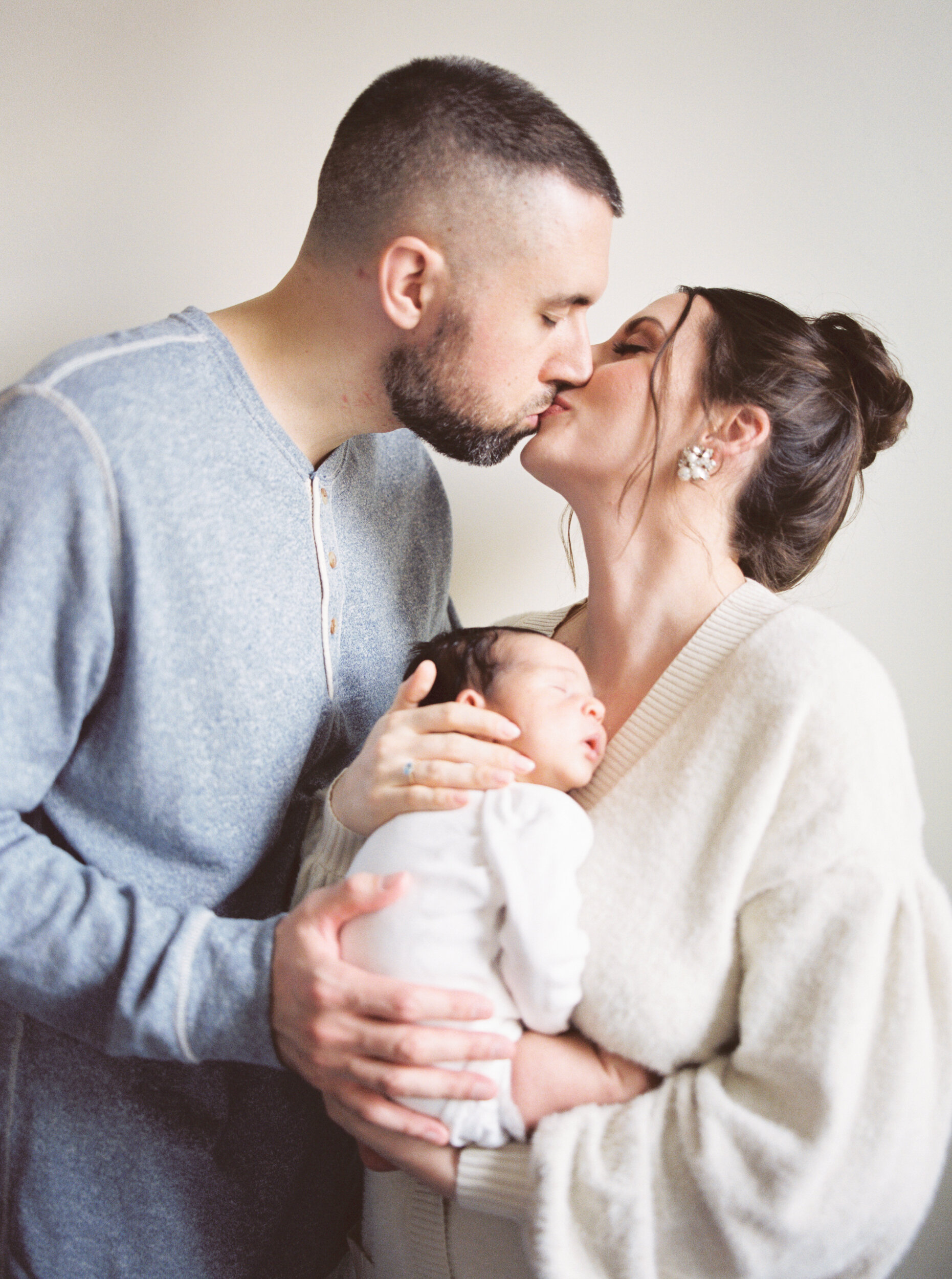 Parents kiss holding their newborn baby 