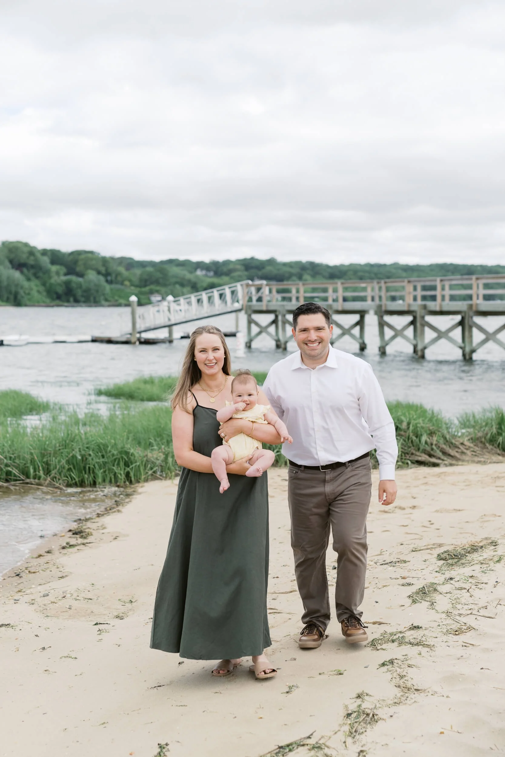 Mom and Dad walking on the beach holding new baby girl for 6-month milestone session