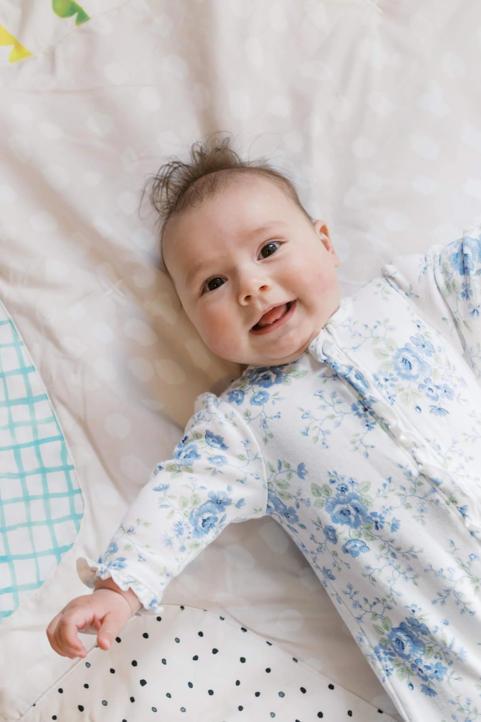 Baby girl smiles up at her parents in her bunny themed nursery during a six month milestone shoot.