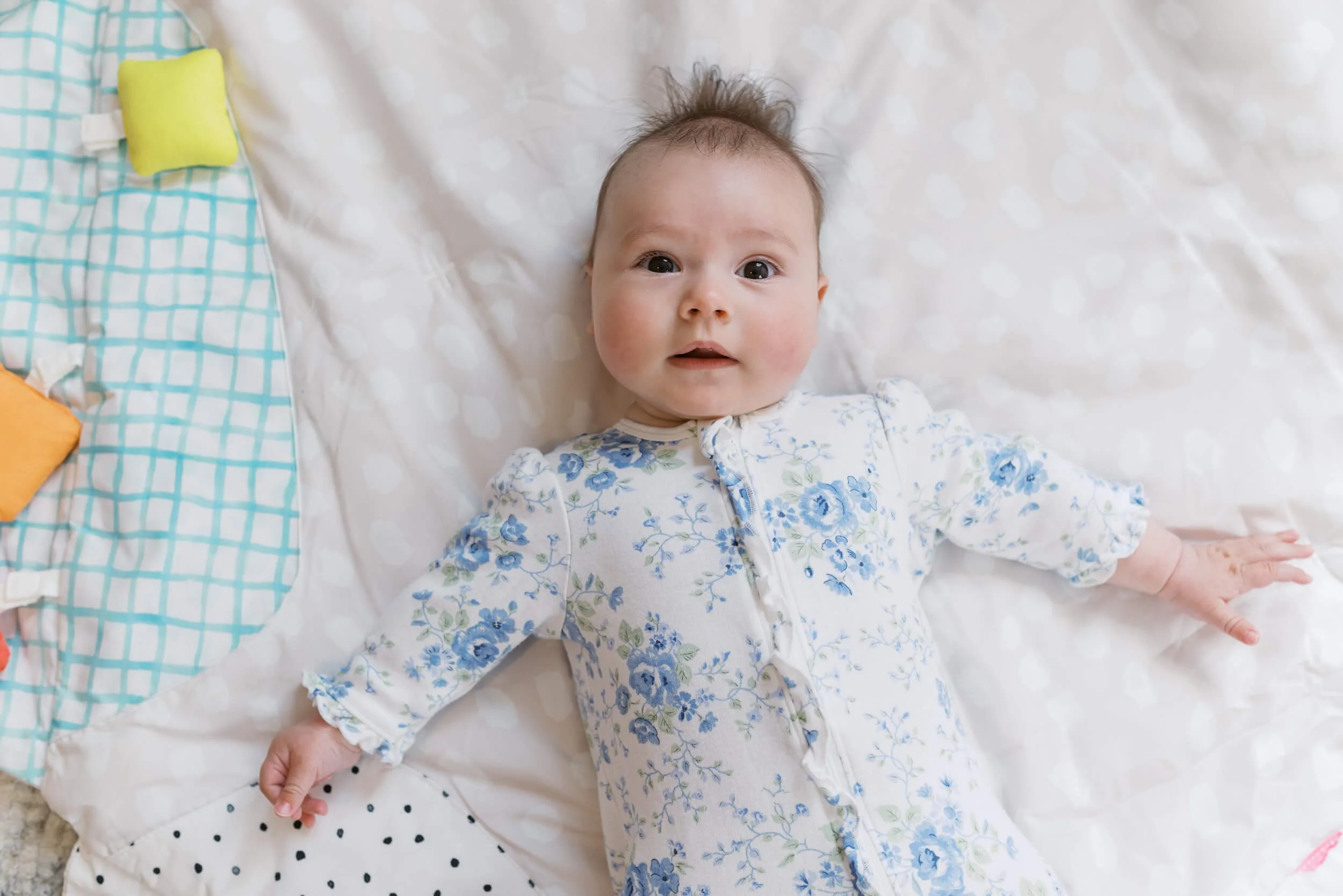 Baby girl smiles up at her parents in her bunny themed nursery during a six month milestone shoot.