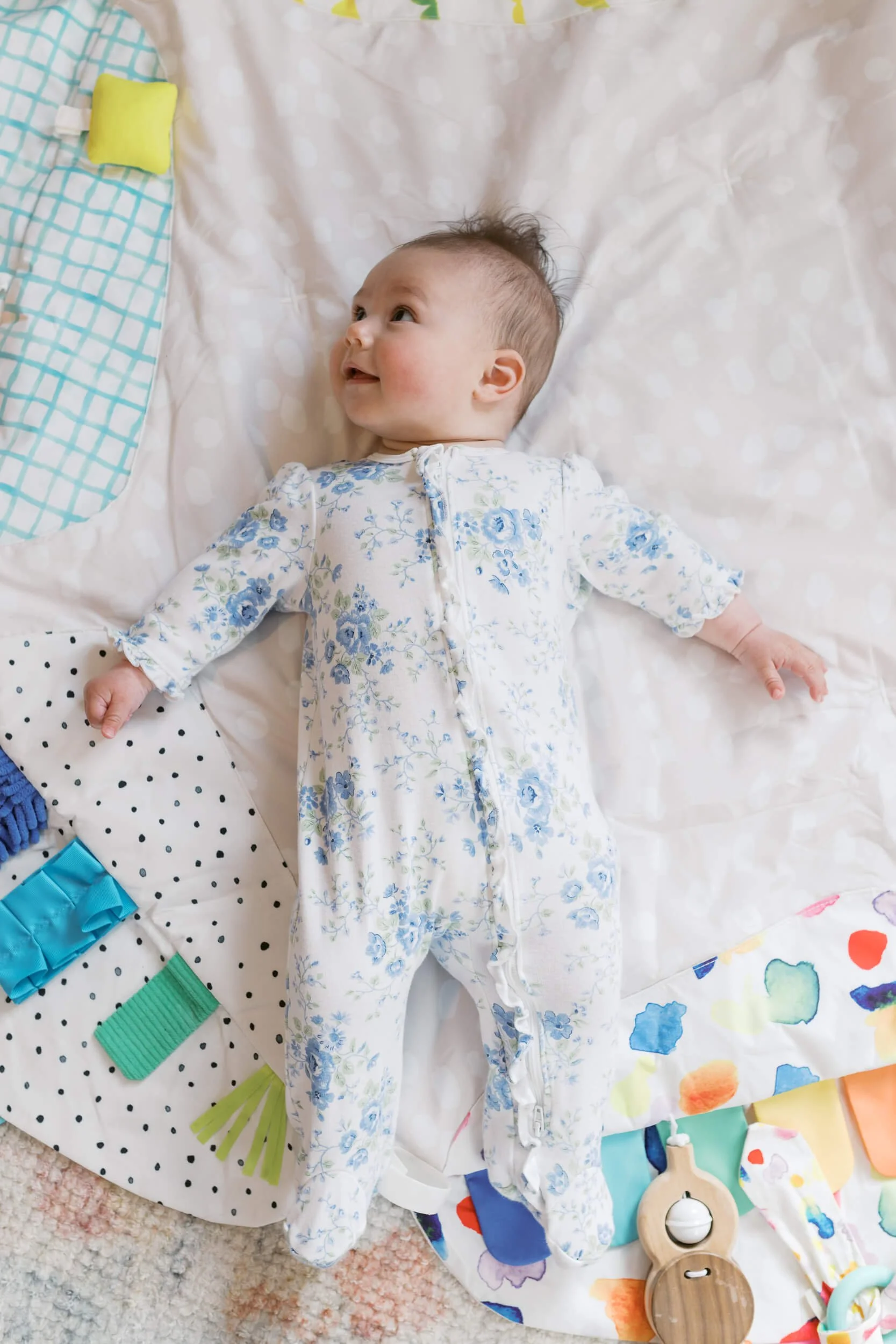 Baby girl smiles up at her parents in her bunny themed nursery during a six month milestone shoot.