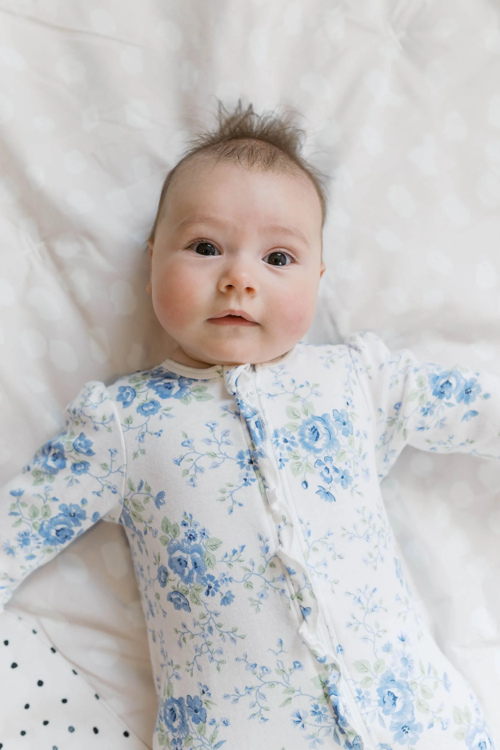 Baby girl smiles up at her parents in her bunny themed nursery during a six month milestone shoot.