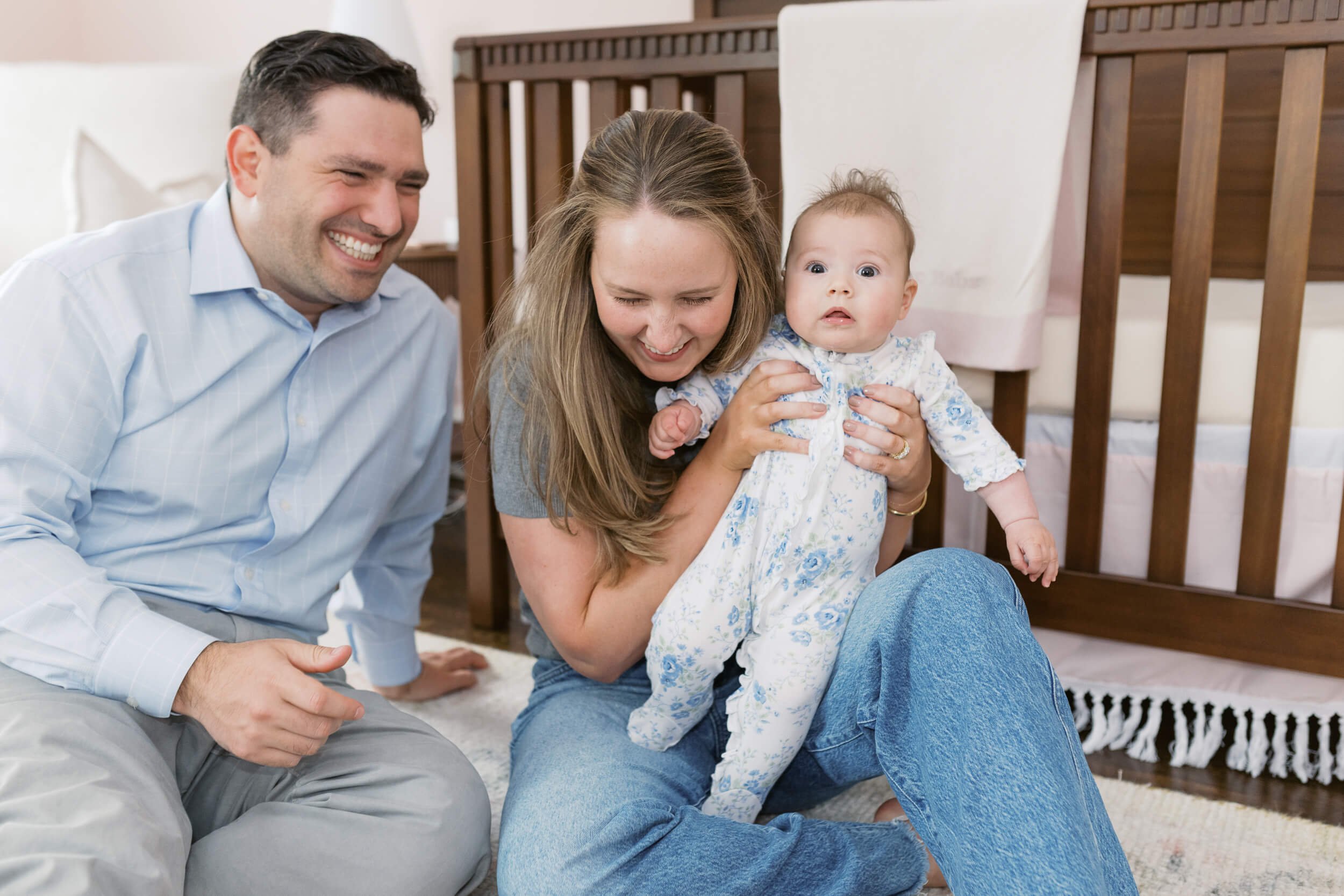 Mom and Dad laughing Mom and dad sit together on the nursery floor for their daughter's six-month milestone session.