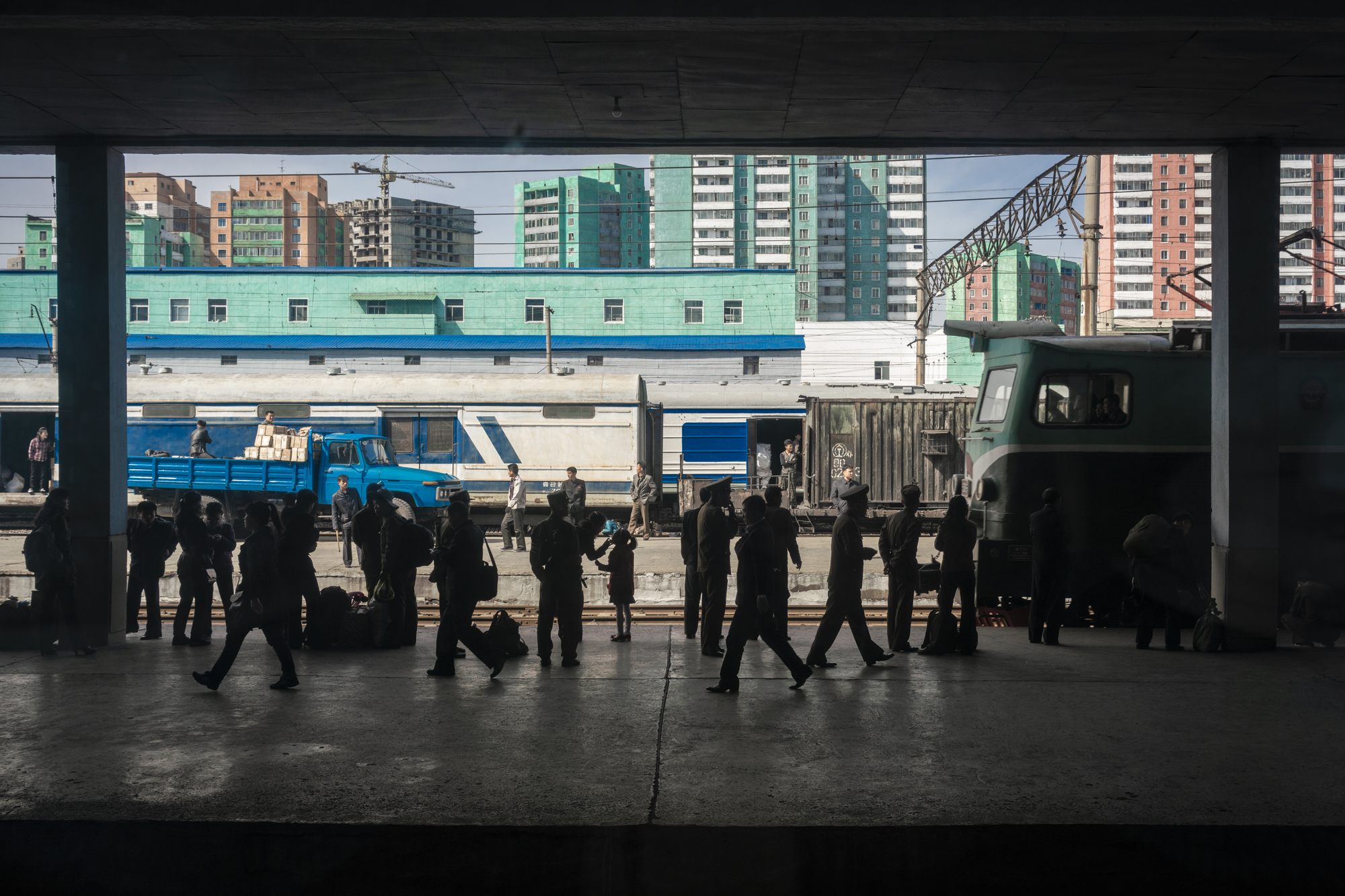 North Korean commuters are standing on the platform waiting for the train. The North Korean Railway still utilises old Soviet trains from the mid-20th century.