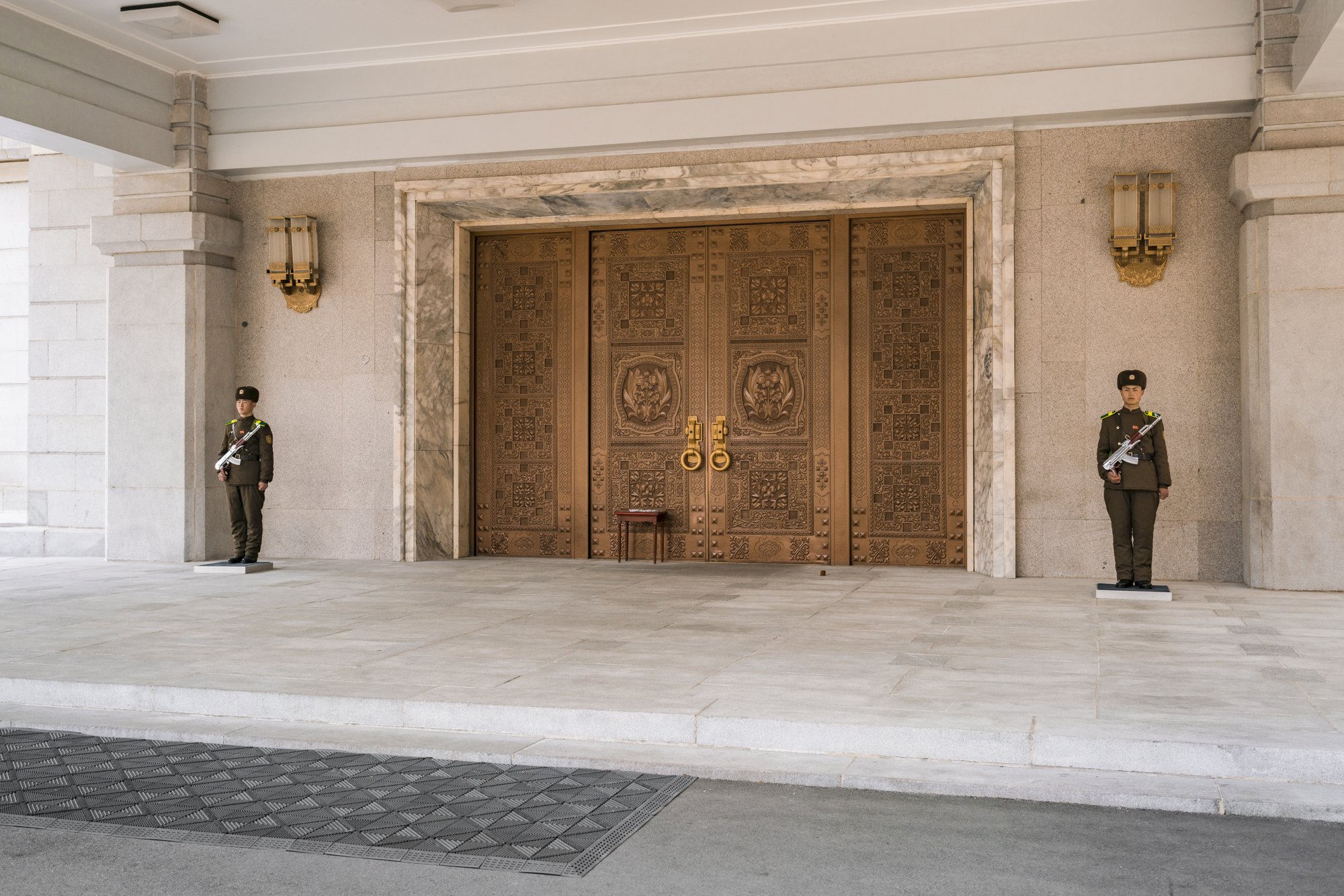 Two motionless North Korean army soldiers with polished silver-plated machine guns guarding the entrance to the Friendship Exhibition Hall complex in the Myohyang Mountains area.